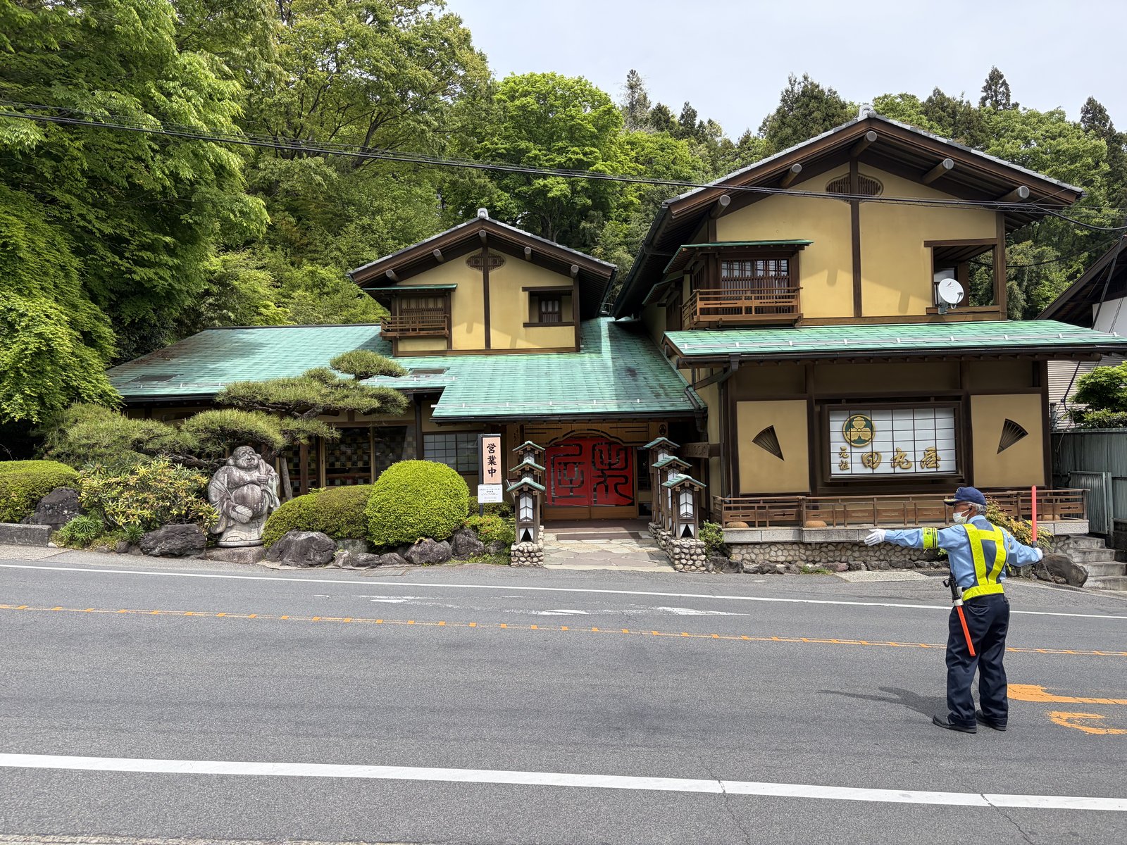 道路向かいから店舗外観・緑屋根・布袋様像・警備員