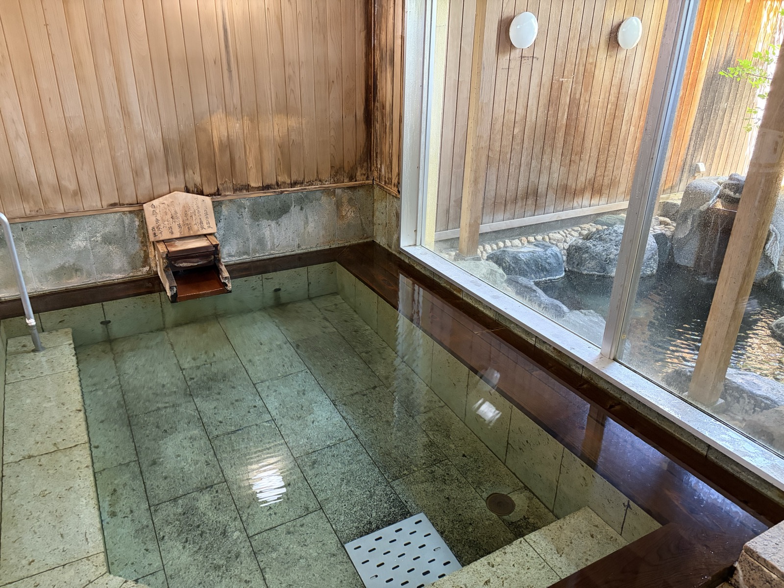 内湯・緑のタイル石床＋木枠の浴槽、洗い場4席、奥の大窓越しに露天が見える