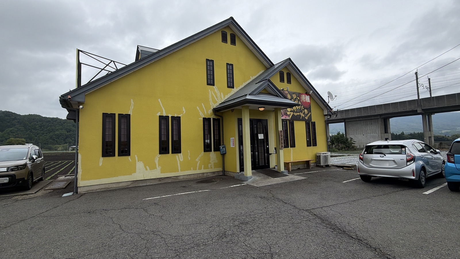 香華 外観・黄色い壁+三角屋根+「ラーメン」の縦看板、駐車場と店本体