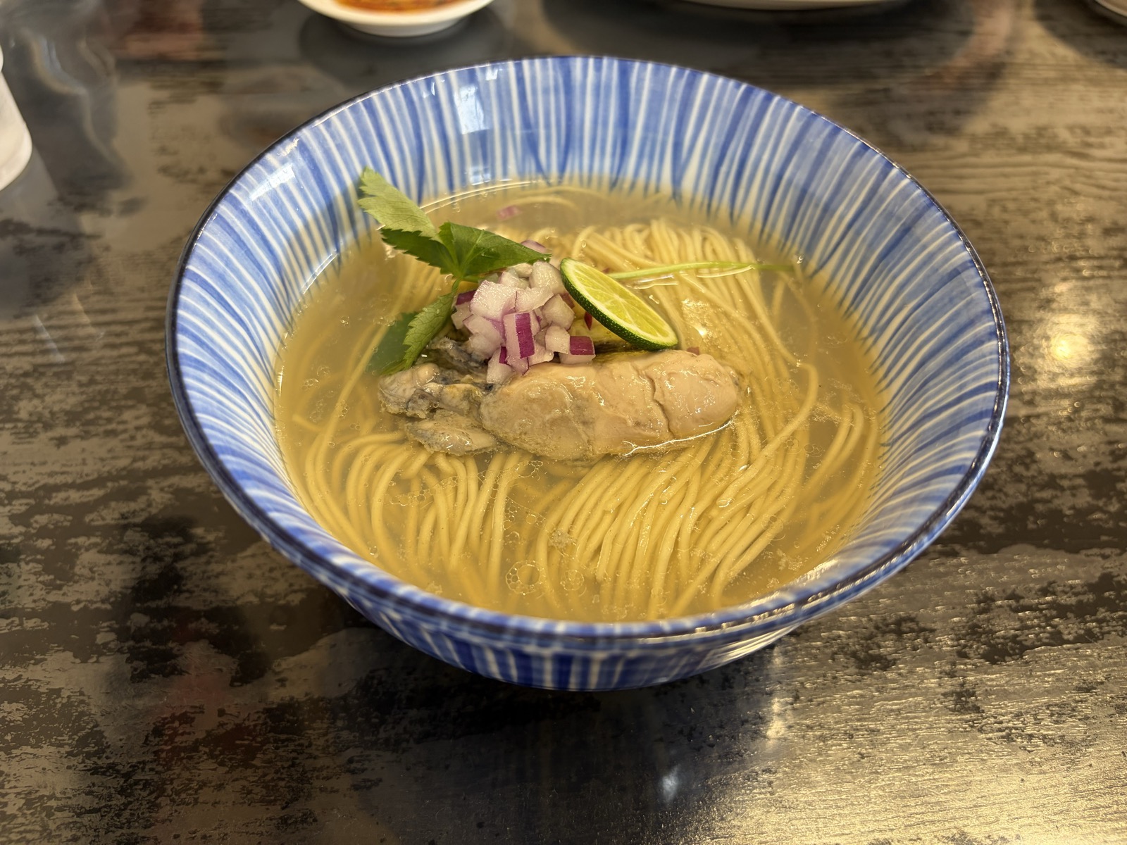 牡蠣らぁめん(塩)1200円・青いストライプの丼に澄んだ塩スープ、中央に大粒の牡蠣+すだち+赤玉ねぎ+三つ葉