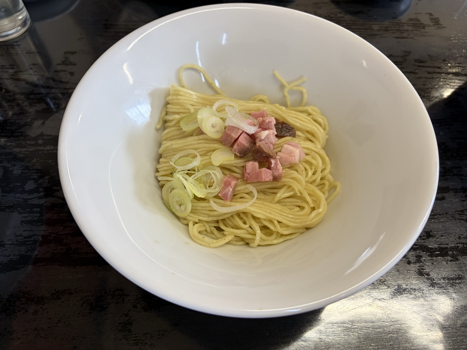 牛脂の和え玉・白い大皿に淡黄色の和え麺+ベーコン状小角+斜めスライスのネギ