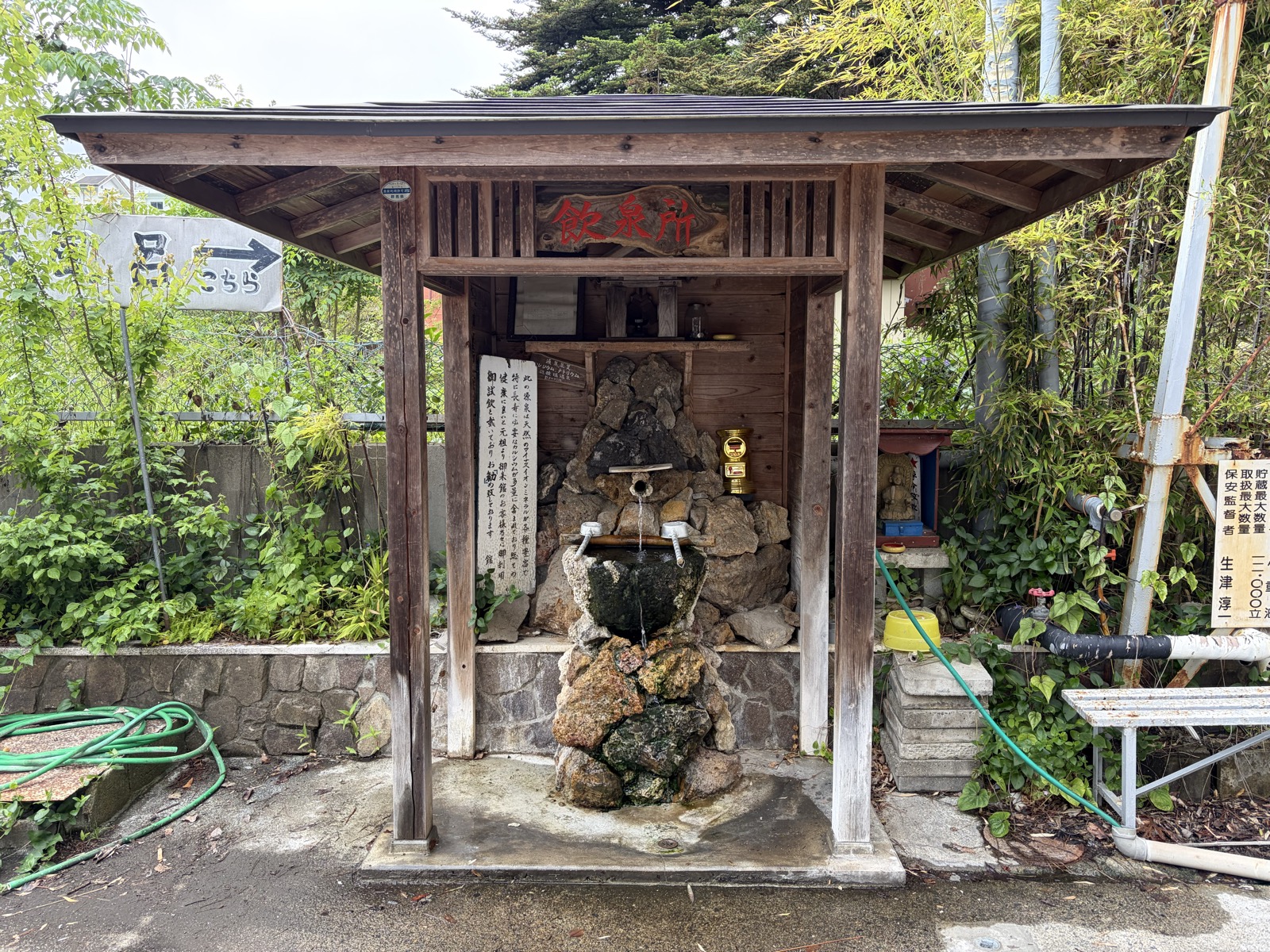 長生館 敷地内の飲泉所・木造の屋根の下に石組みの飲泉口、柄杓と説明板