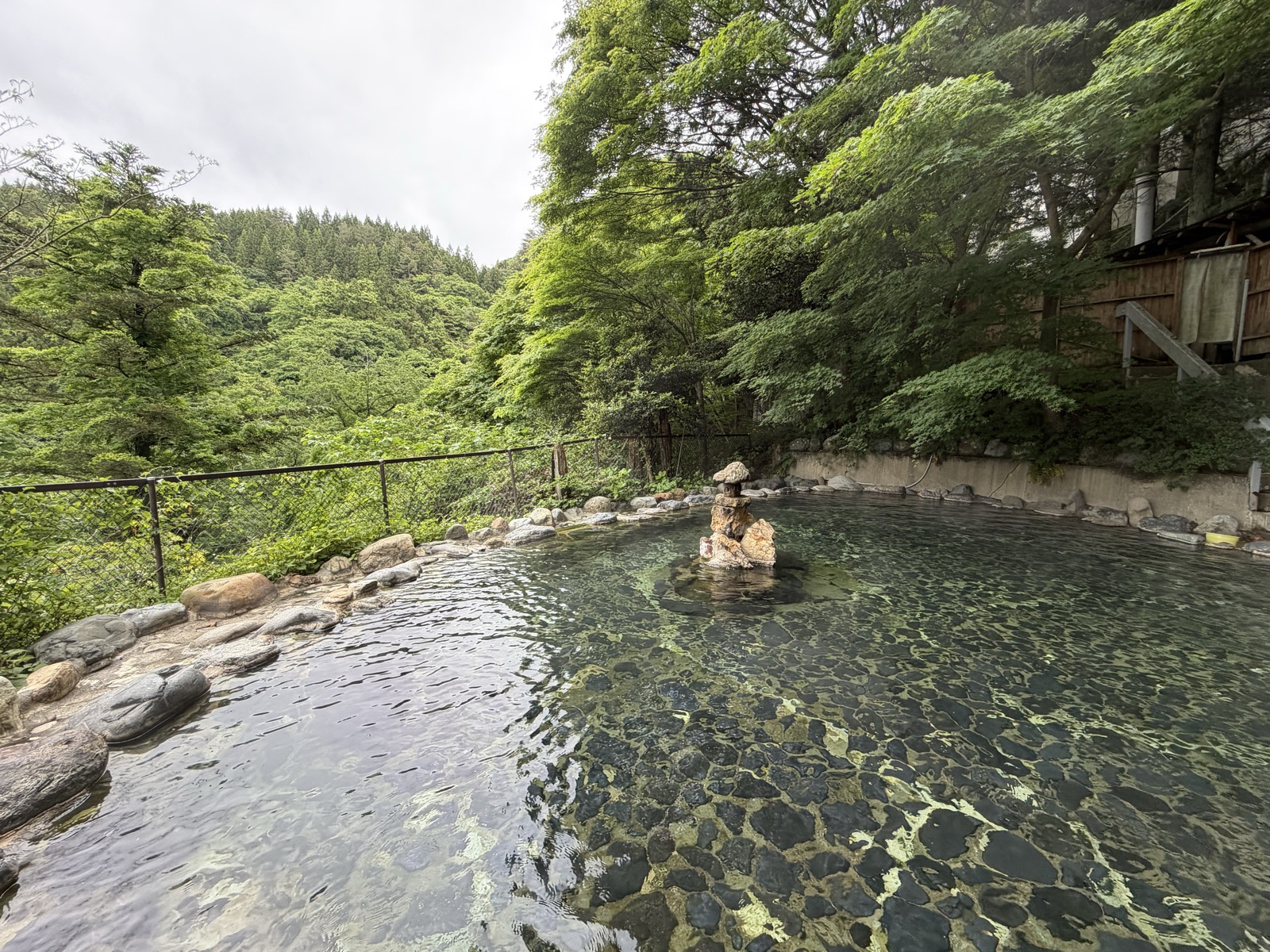野天風呂 別角度・湯口の岩と浴槽全景、奥に山並み