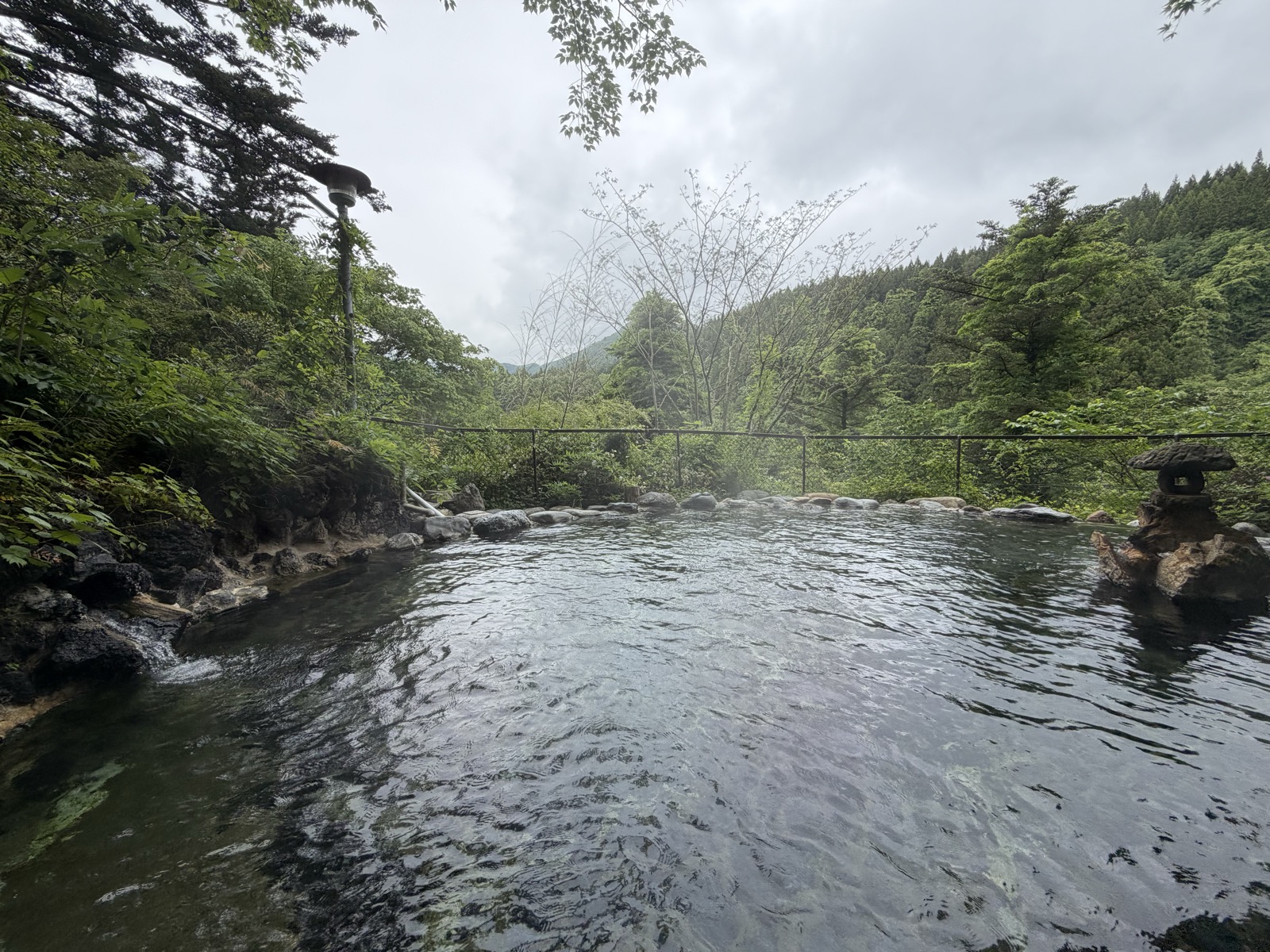 男湯野天風呂・雨上がりの湯気立ち上る、奥の山が霞む静かな構図