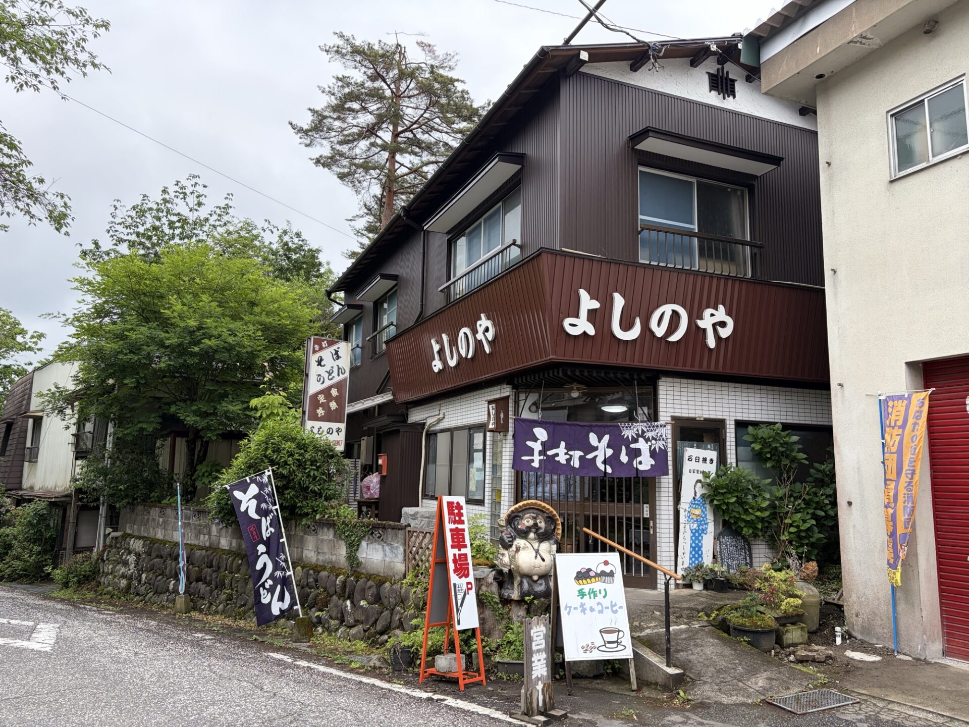 よしのや外観。暖簾と「手打ちそば」の幟、信楽焼のたぬきが目印