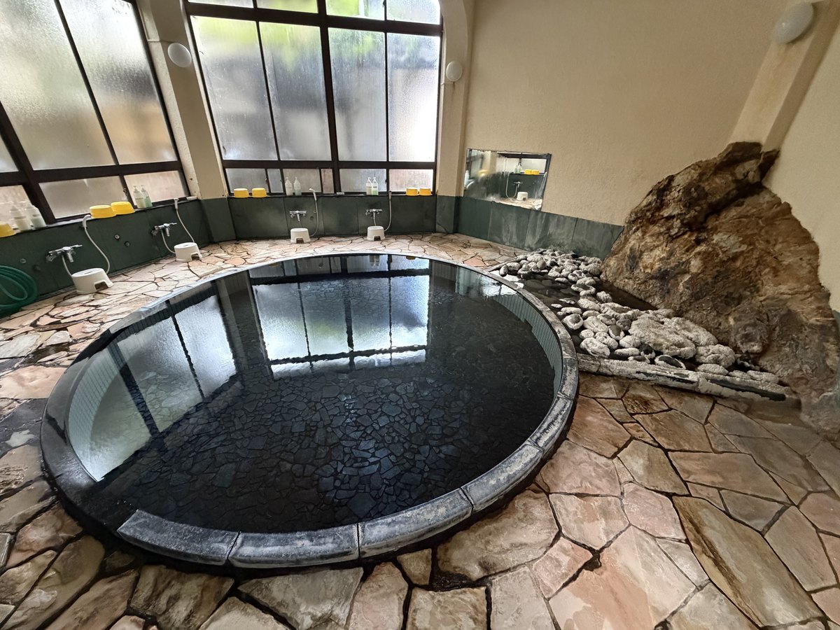 湯面|黒石の浴槽に張られた無色透明の湯。縁から静かに溢れる