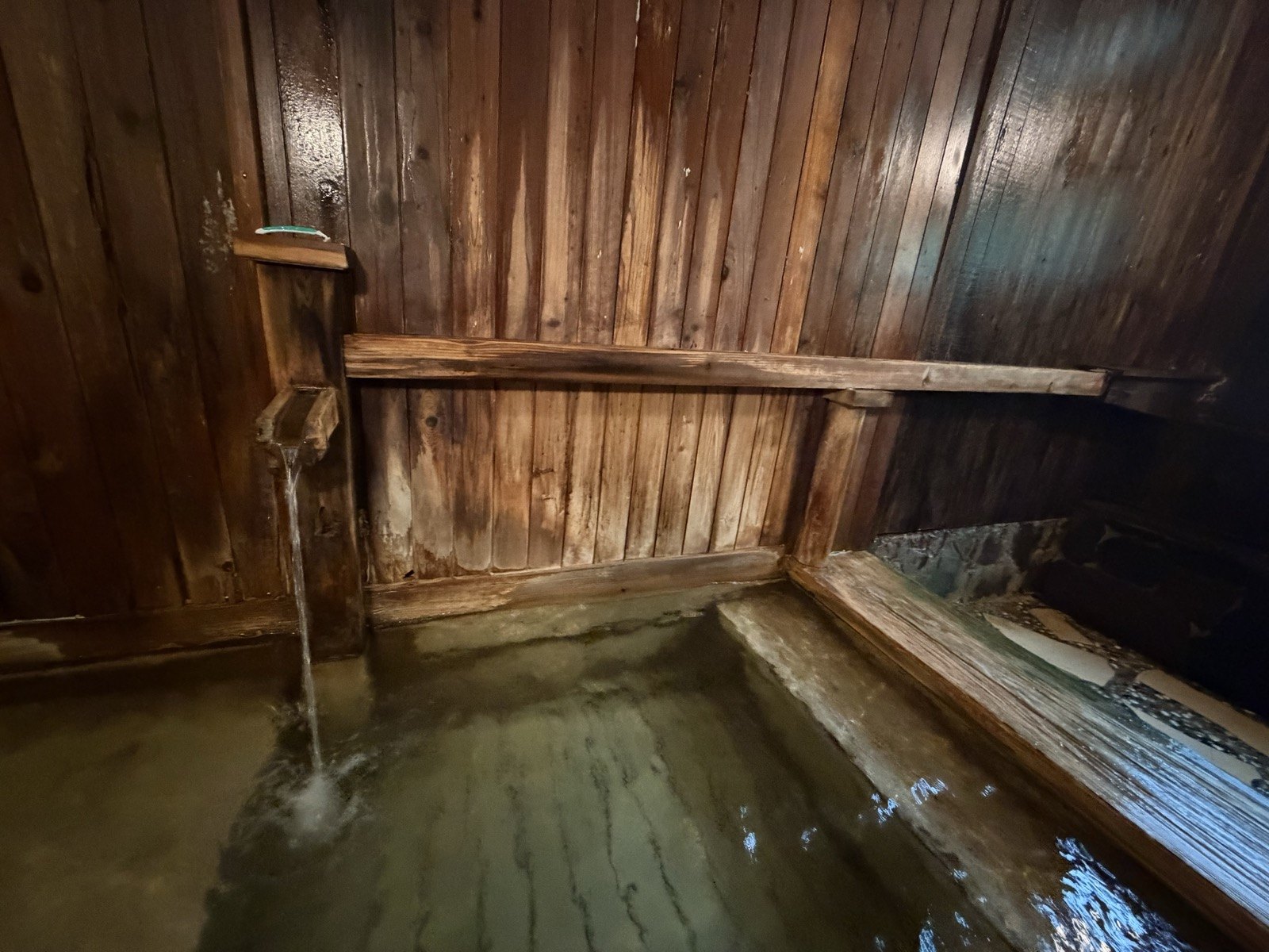 木の湯口からとろりと注がれる源泉。湯面は緑がかってやわらかい