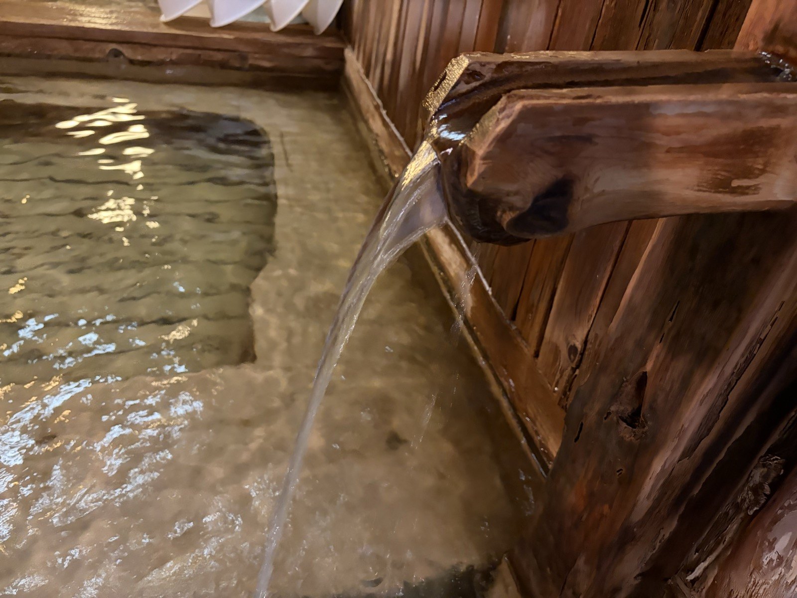 石を敷いた浴槽の底。湯口から落ちる湯と、緑がかった湯のグラデーション