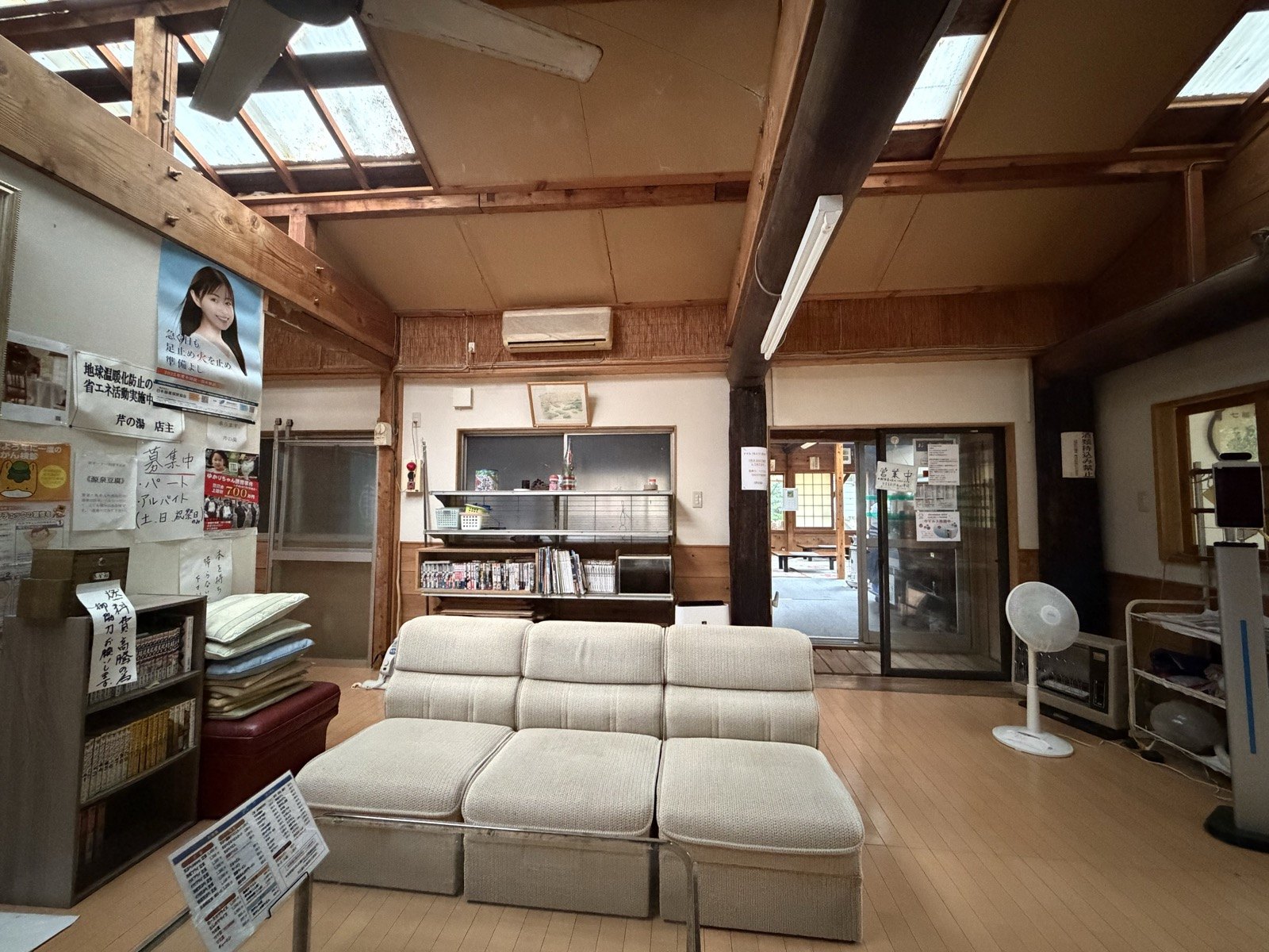 天窓から光が落ちる広い休憩処。畳とソファ、扇風機の昭和感