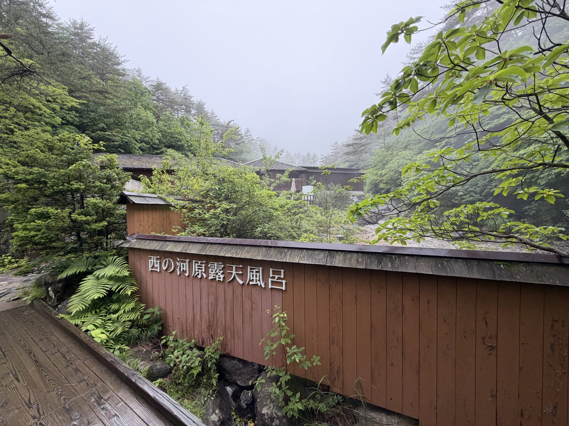 「西の河原露天風呂」の木塀サイン。霧の山あいに立つ