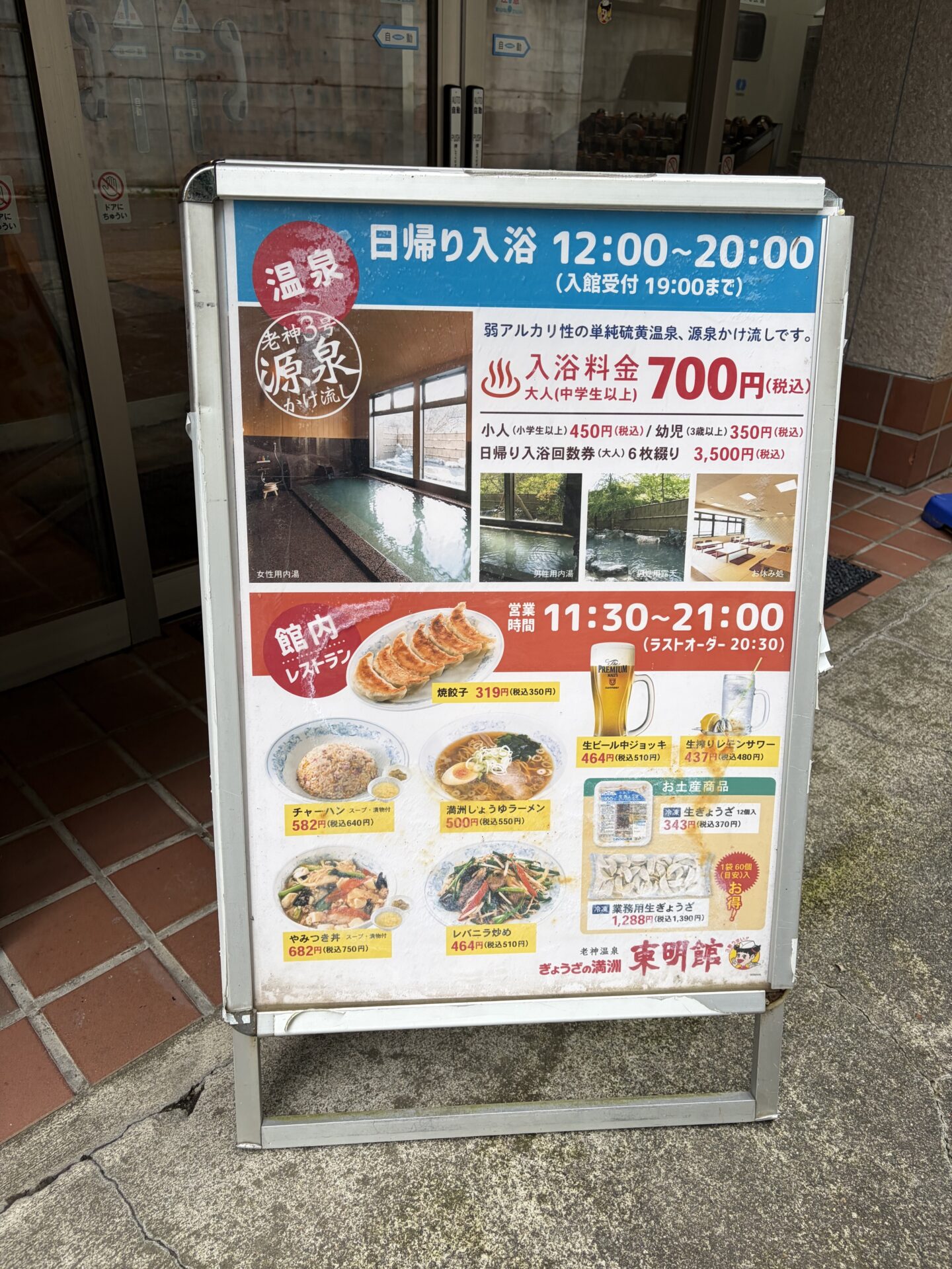 入口の料金看板。日帰り入浴12:00〜20:00・700円、館内レストラン11:30〜21:00とメニュー写真
