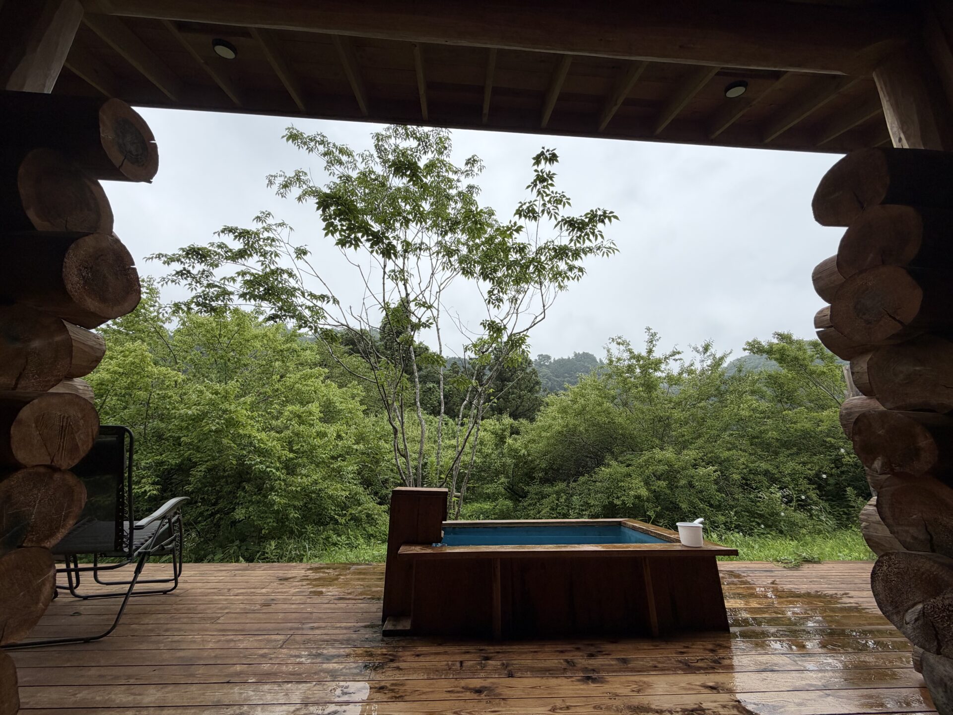 デッキの屋根の下から望む外気浴の眺め。雨に濡れた木々と空