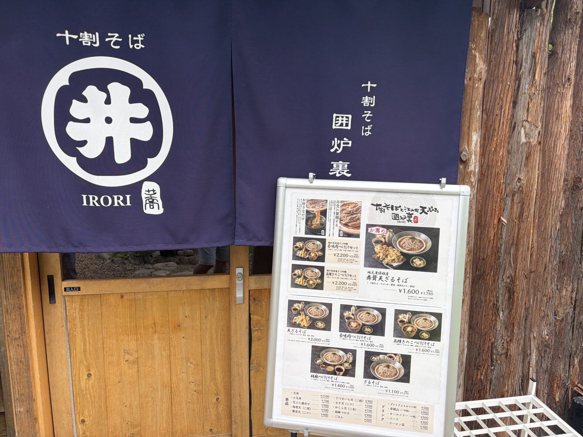「十割そば 囲炉裏」の紺の暖簾(井桁マーク)と、店頭の立て看板メニュー