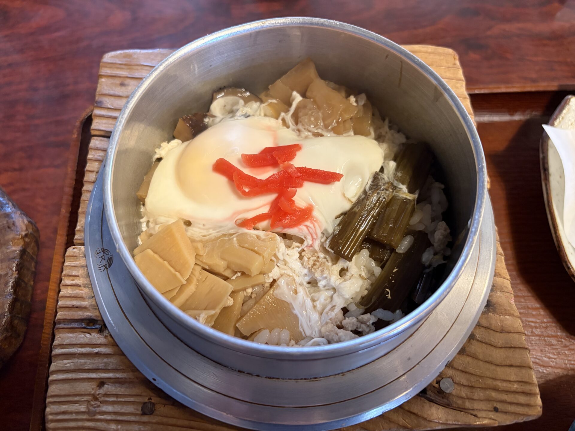 蓋を開けた山菜釜飯。たけのこ・山菜・半熟玉子・紅しょうがが乗る炊きたての釜飯