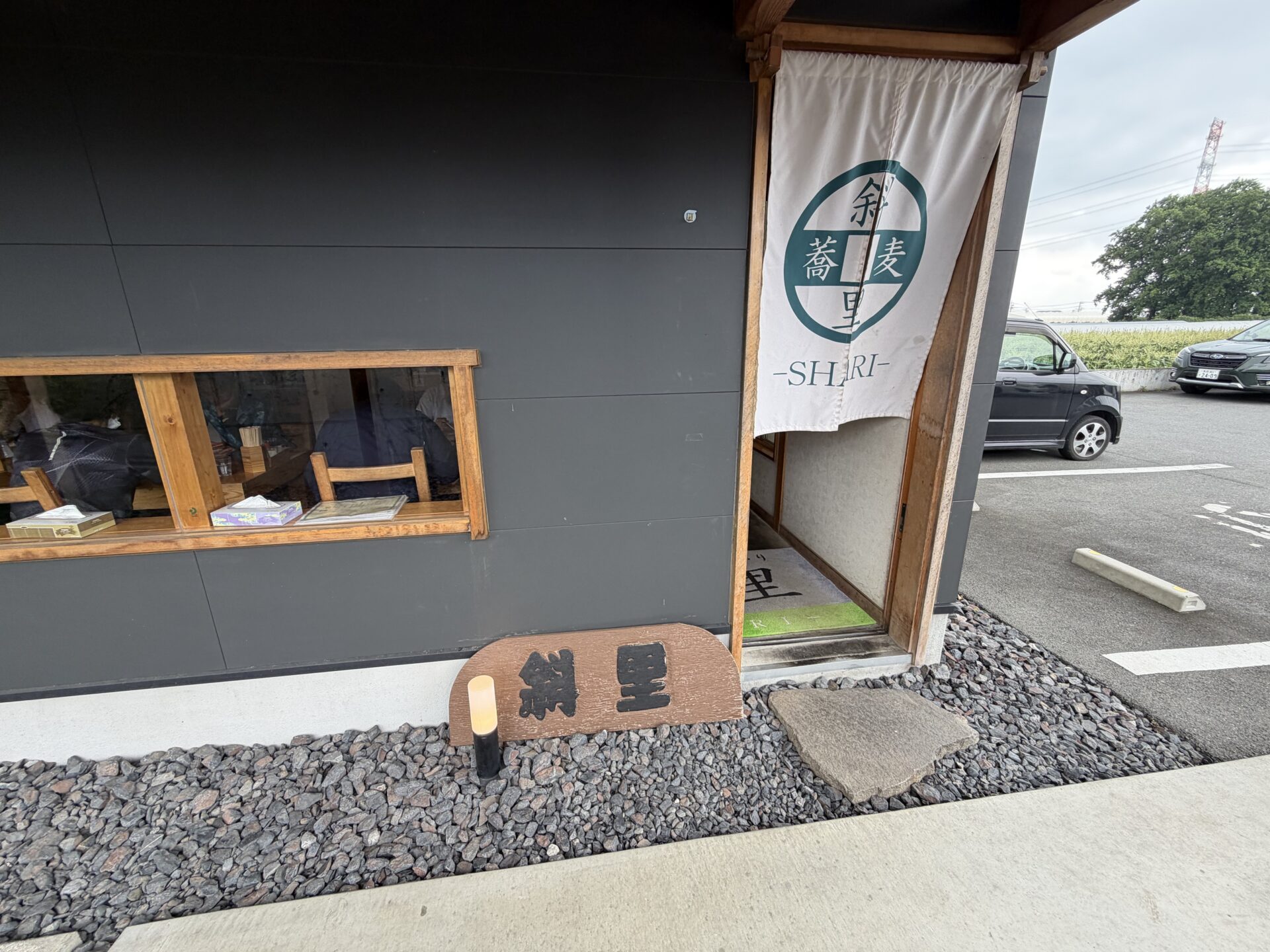 斜里の外観。黒壁×木の庇に「斜里 蕎麦 -SHARI-」ののれんと木の看板