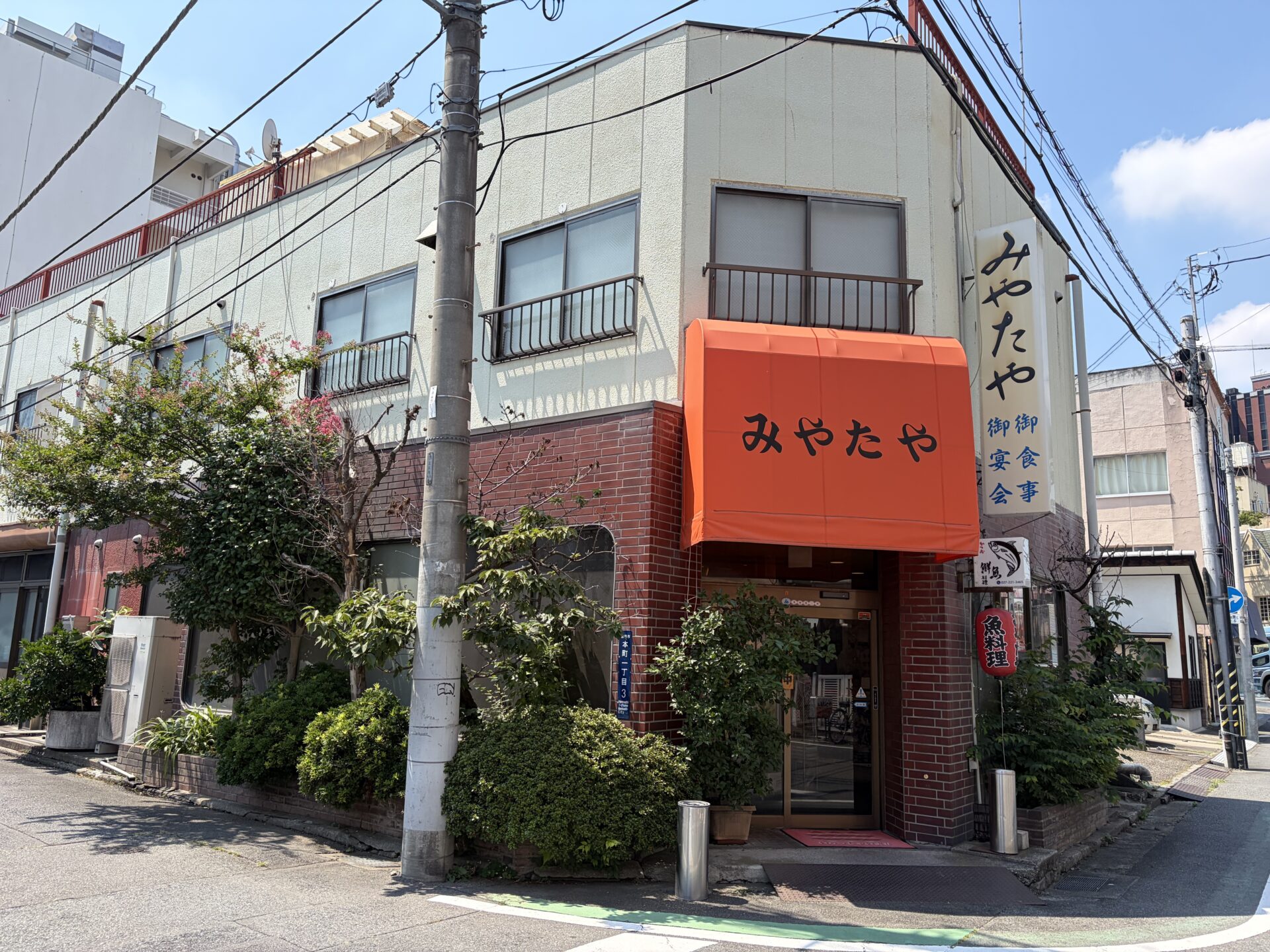 みやたや外観。オレンジの日よけに「御食事・御宴会」の縦看板、軒先には「魚料理」の赤提灯