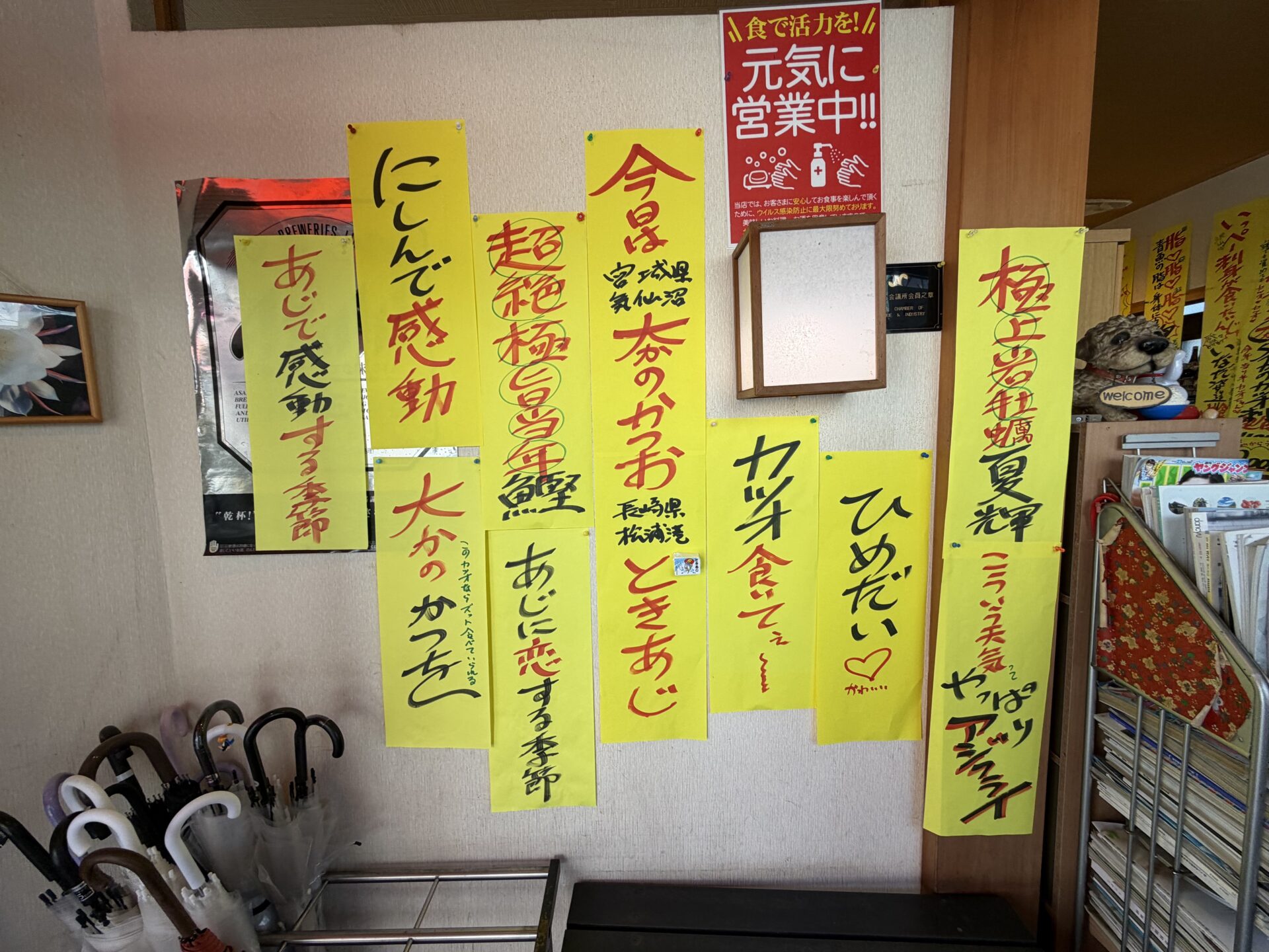 入口横の壁一面に貼られた手書きの黄色いPOP。「今日は宮城県気仙沼 本のかつお」「長崎県松浦港 ときあじ」「極上岩牡蠣 夏輝」の文字