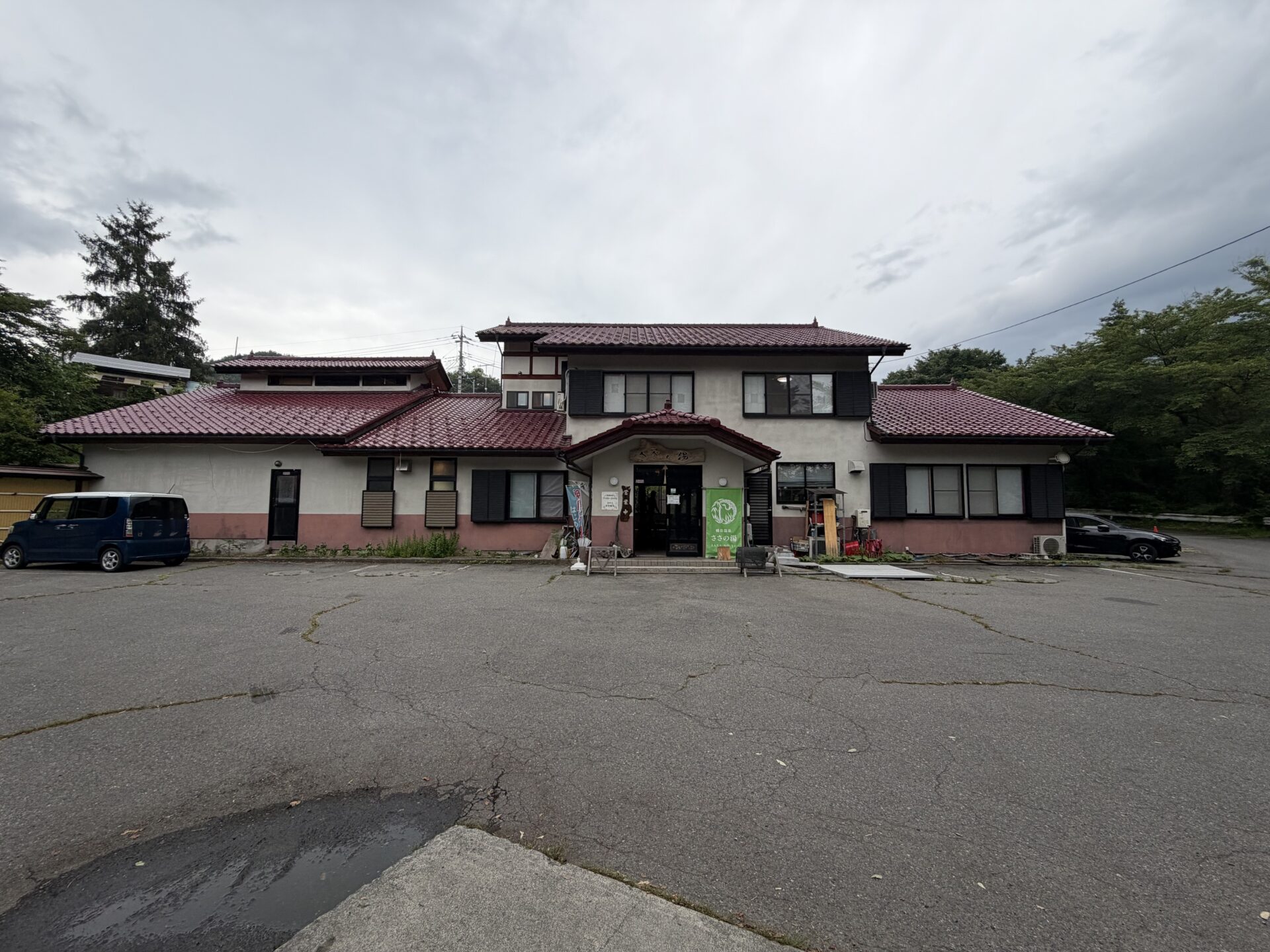 ささの湯の外観。赤瓦屋根の二階建て、広い駐車場。朝で人影はまばら