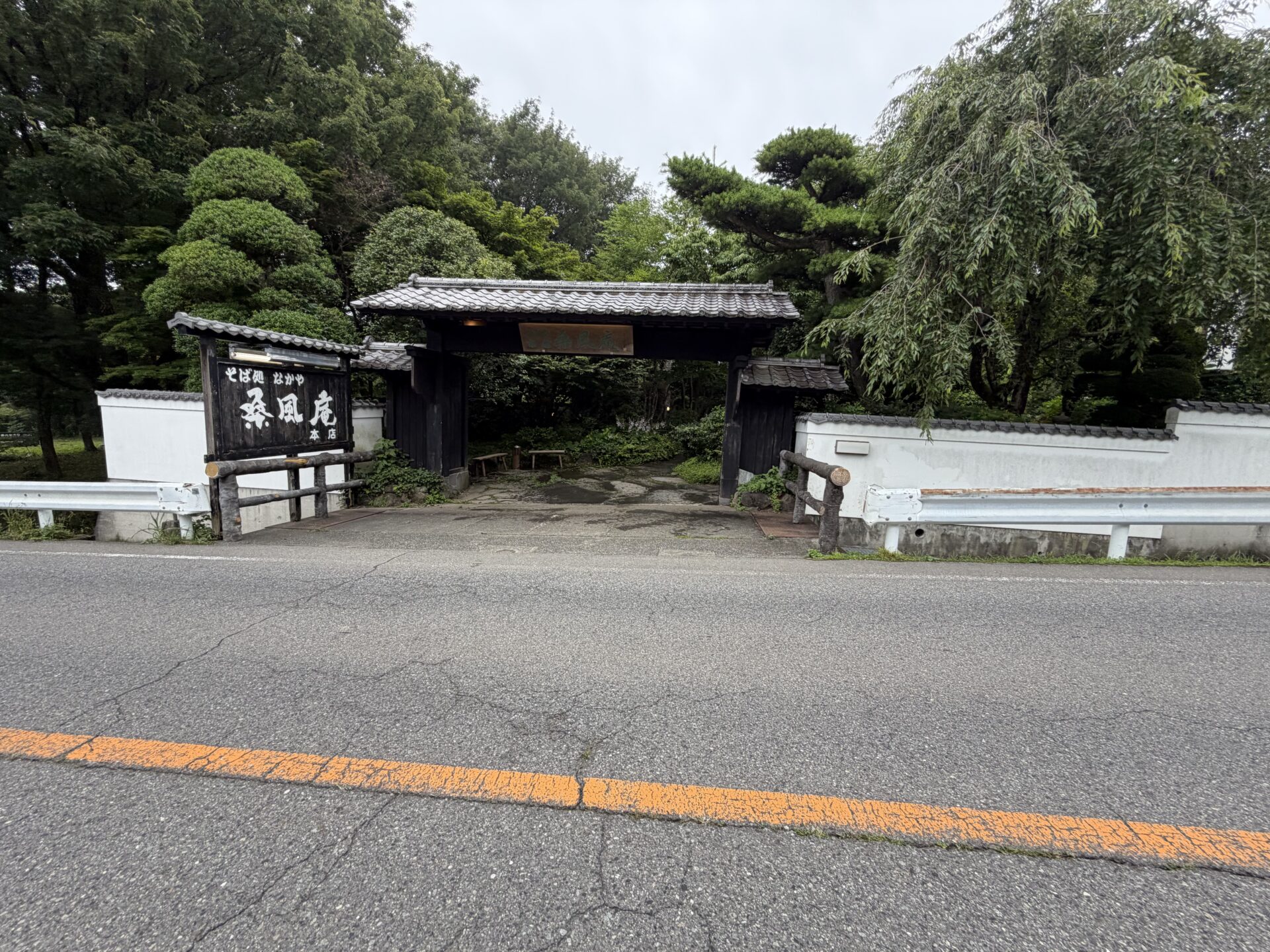 桑風庵本店の外観。黒塀に瓦屋根の門、「そば処 なかや 桑風庵 本店」の看板。門の奥は緑の参道