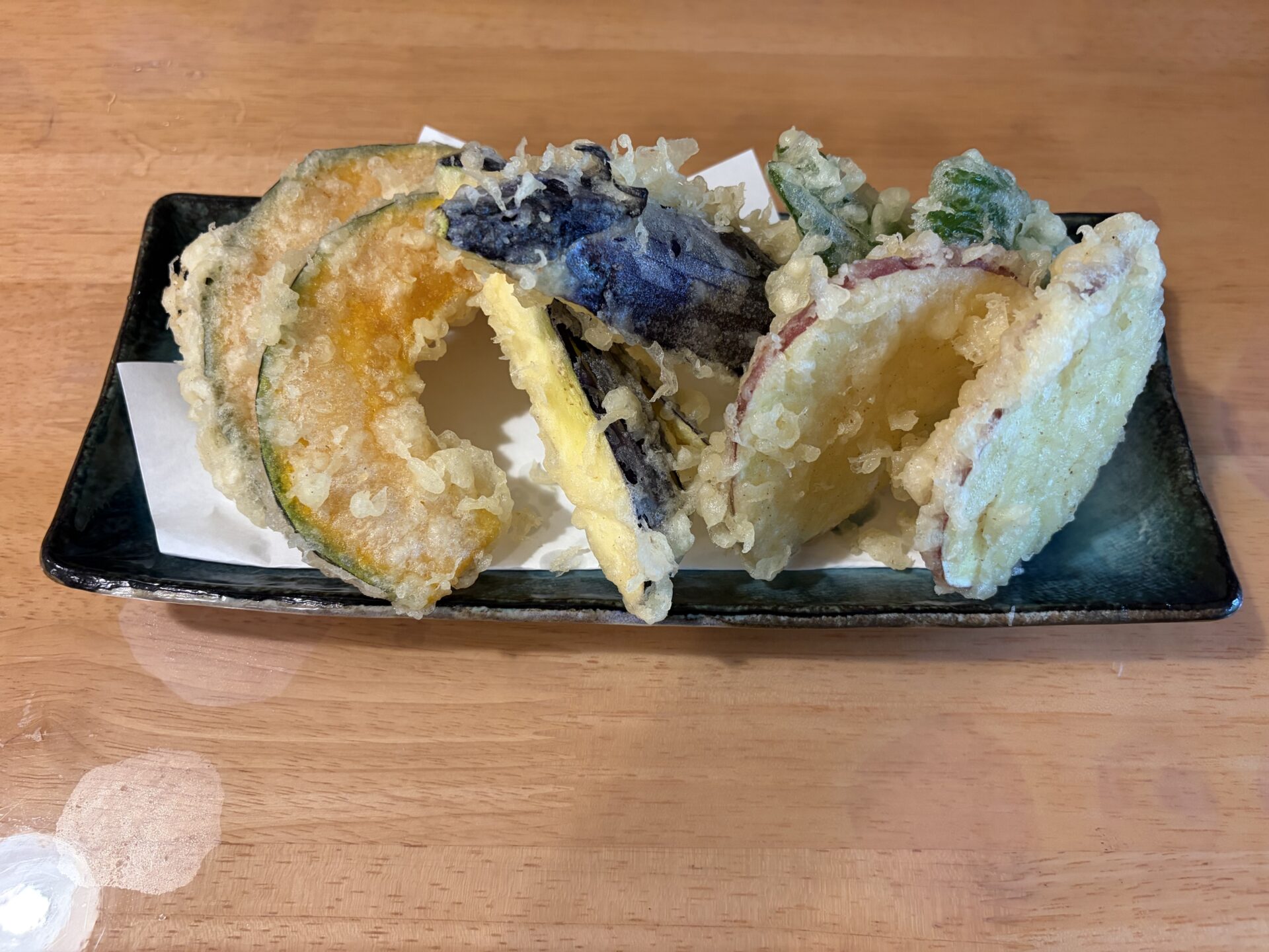野菜天ぷら。黒い長皿に、かぼちゃ・なす・さつまいも・ピーマンの天ぷら。衣は薄く色白