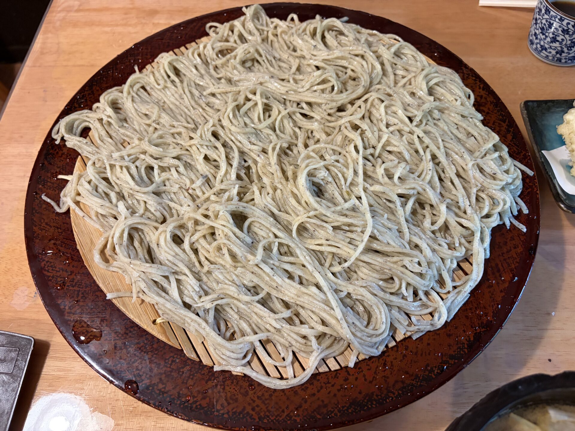 七合のそば。大きな丸いせいろに盛られた、やや灰色がかった麺。そば殻の黒い粒が見える