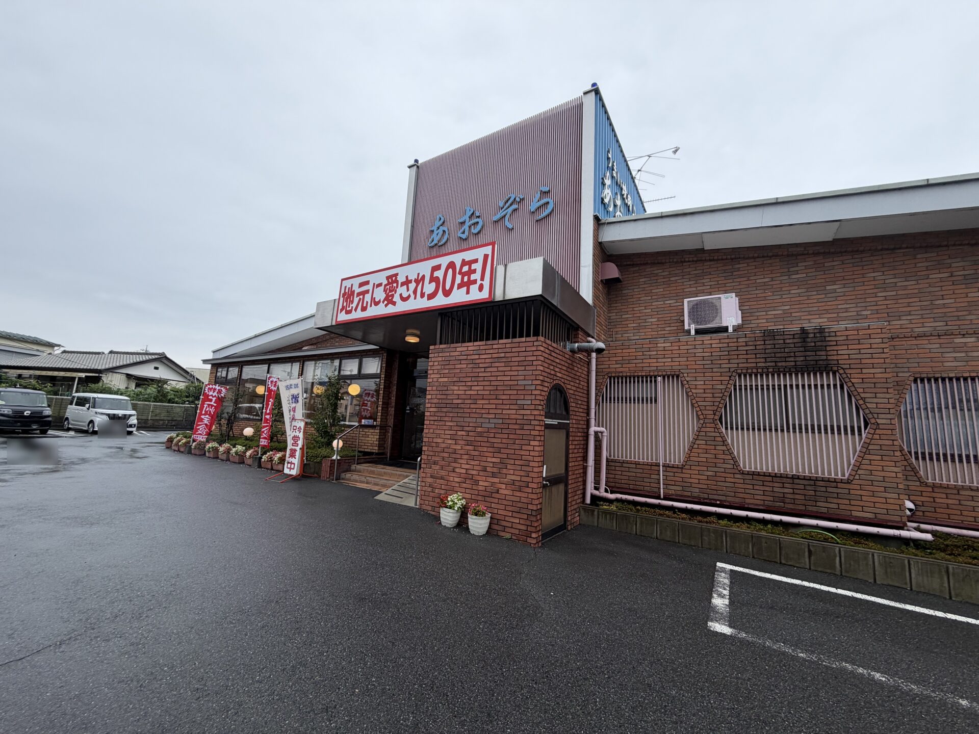 レンガ造りに青い看板。「地元に愛され50年！」の文字が堂々と掲がる