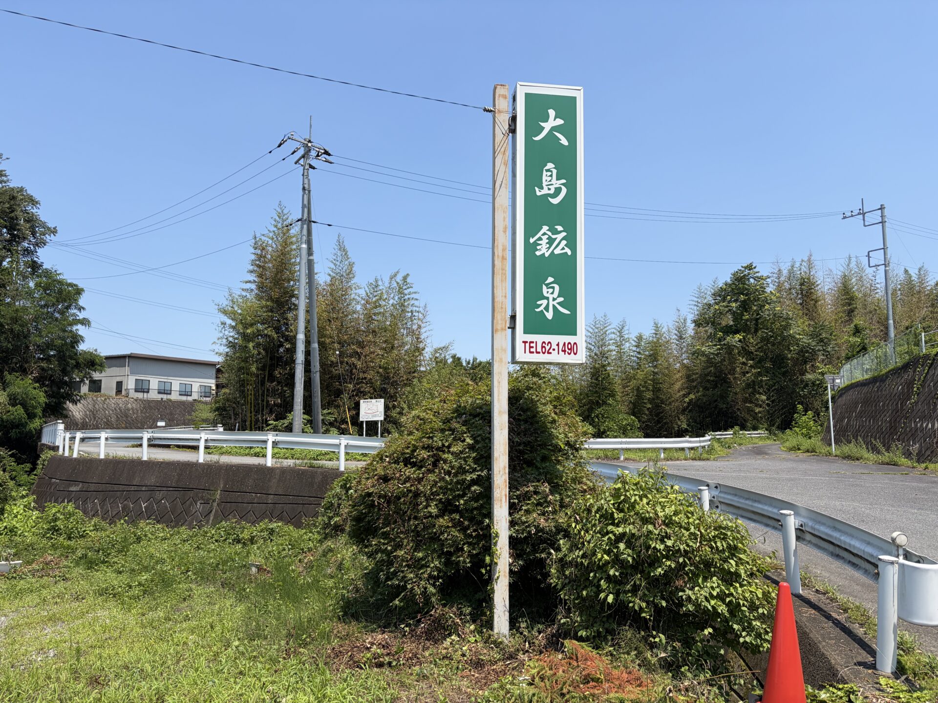 道路脇の緑の縦看板「大島鉱泉 TEL62-1490」。ここを目印に脇道へ入る