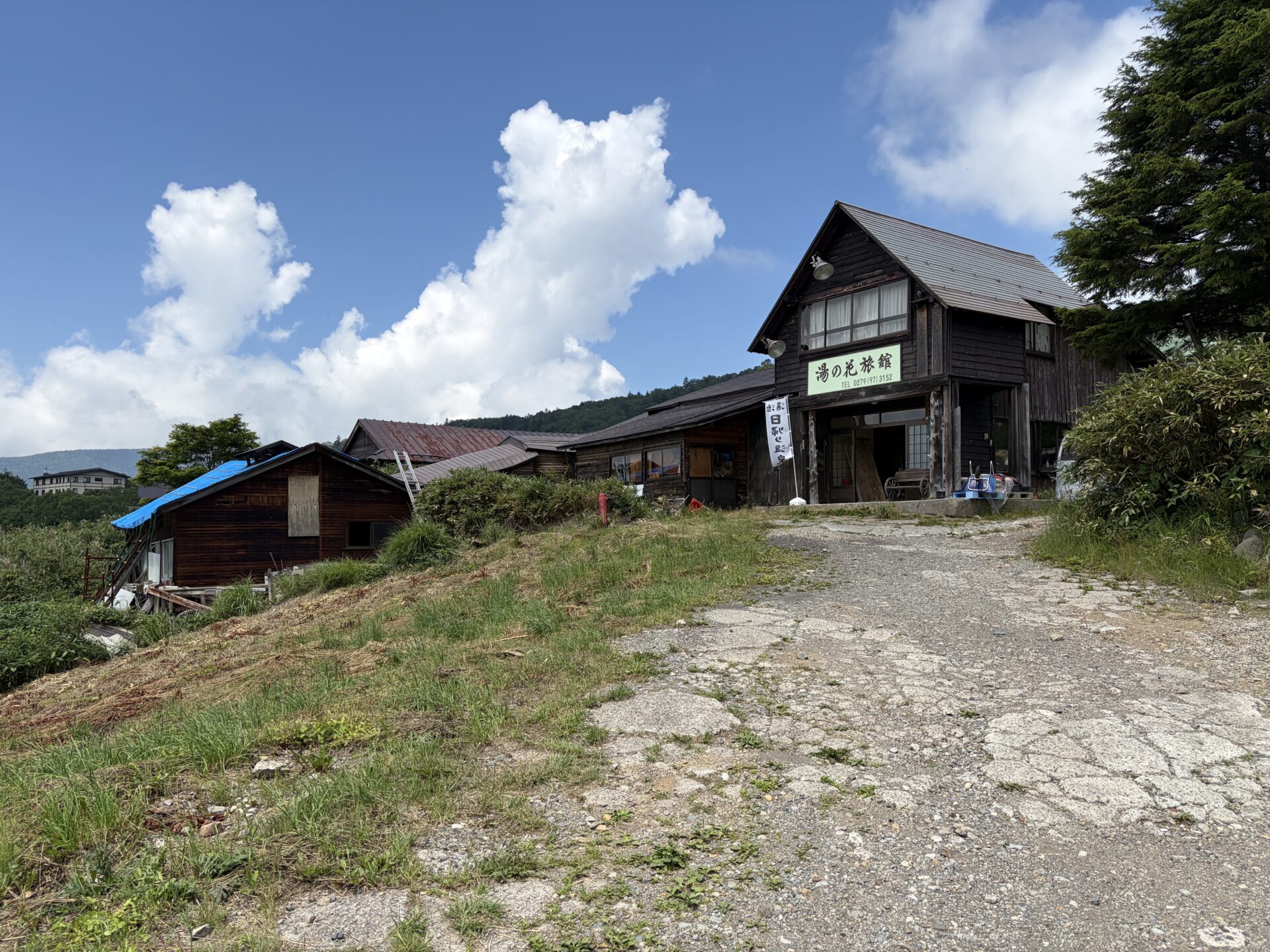 青空と入道雲を背に建つ湯の花旅館の木造の外観・施設名看板