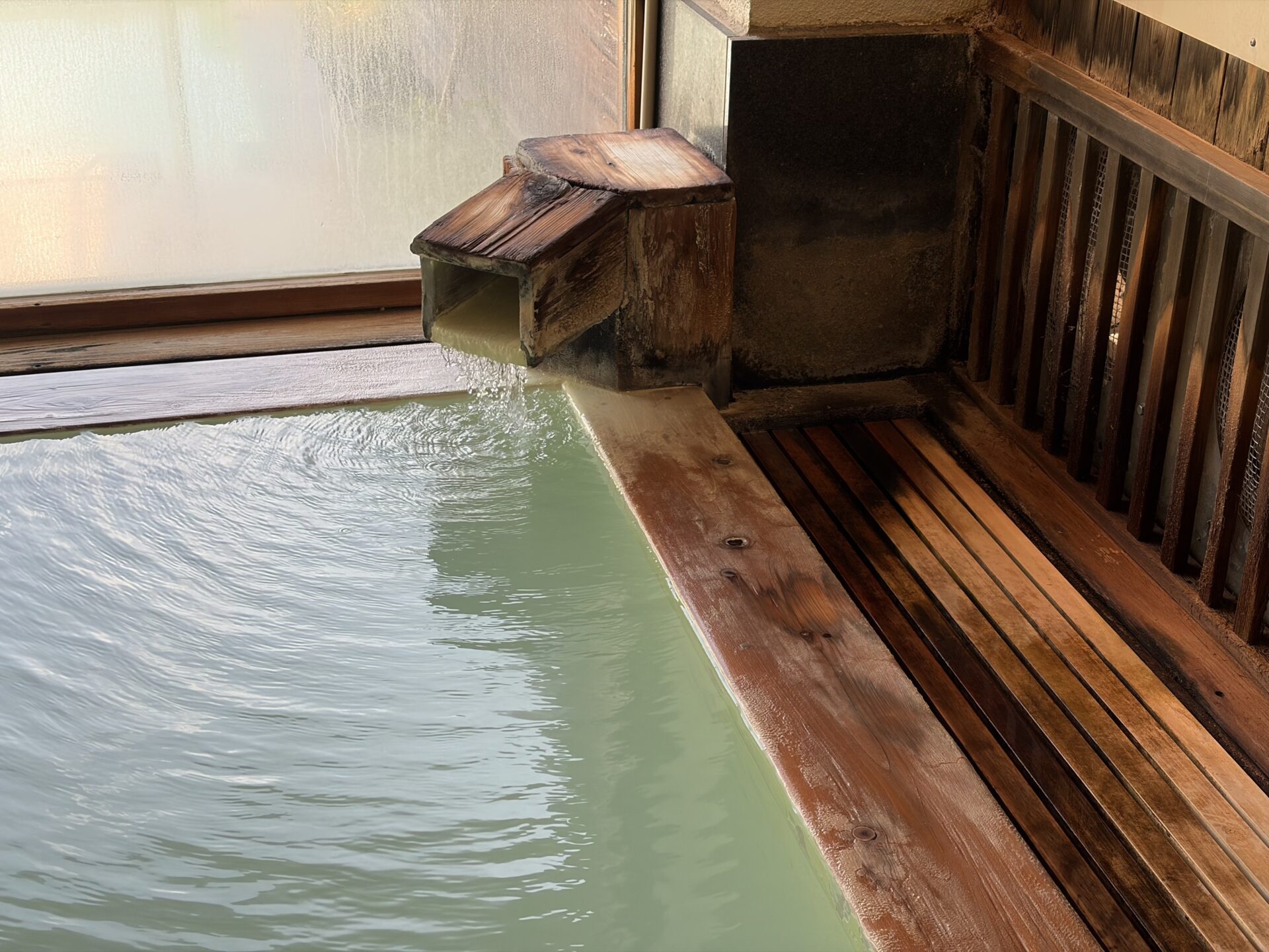 木の縁と湯口。青緑に濁った露天の湯
