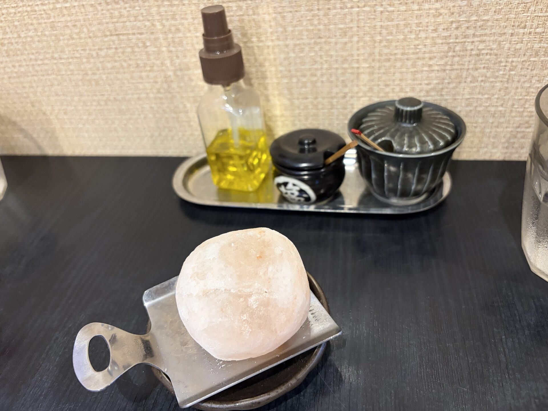 卓上のオリーブオイルスプレー、岩塩の塊、薬味入れ。岩塩はおろし金で自分で削るスタイル