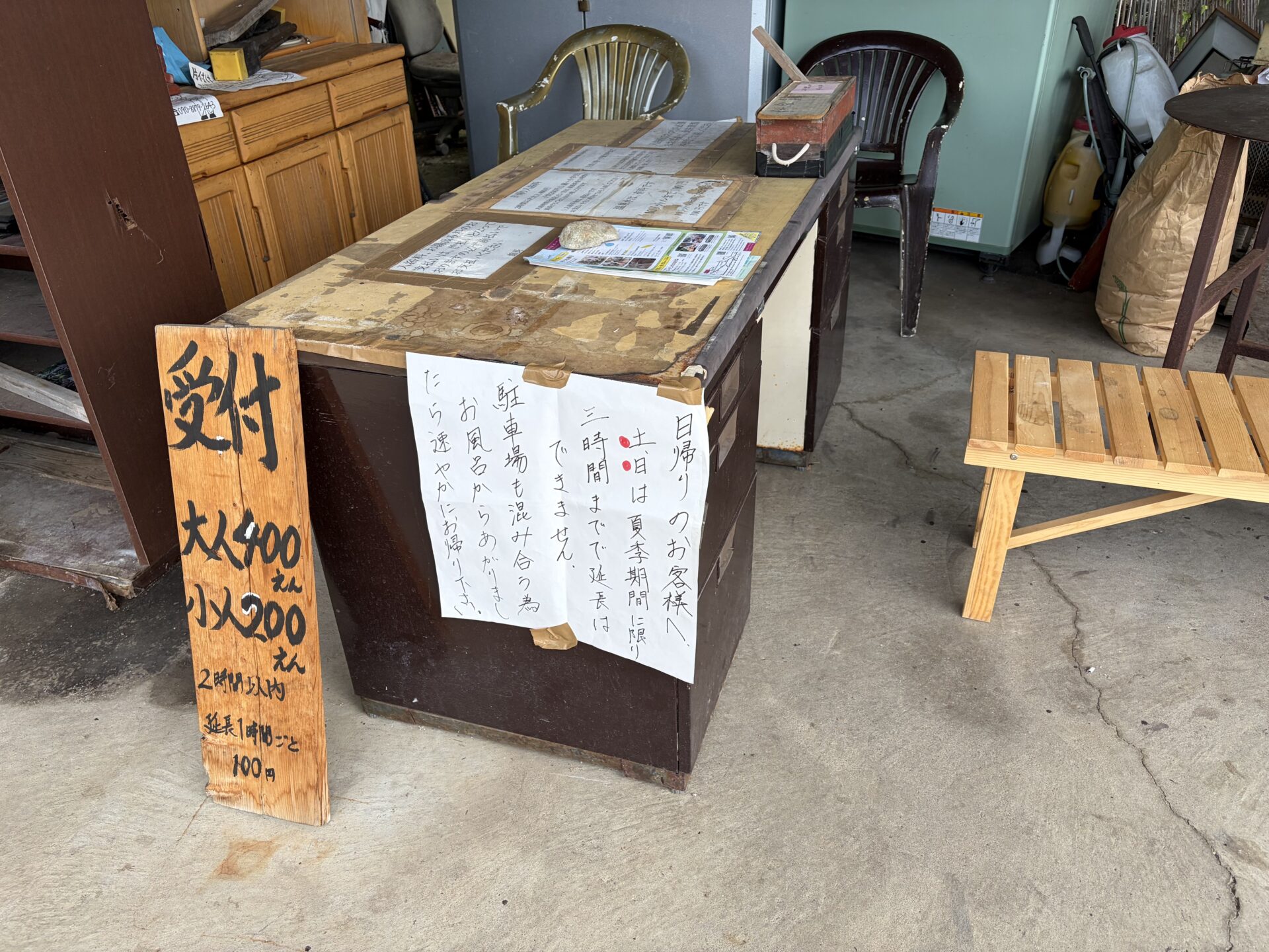 無人の受付。手書きの木札と「日帰りのお客様へ」の貼り紙