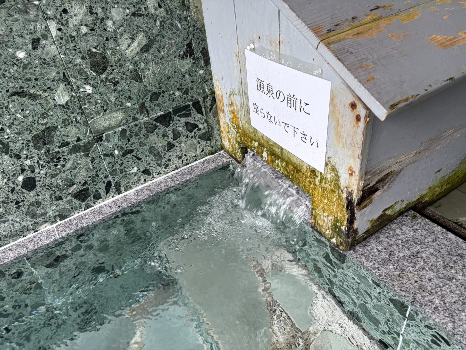 源泉投入口。「源泉の前に座らないで下さい」の貼り紙と、絶えず注がれる無色透明の湯