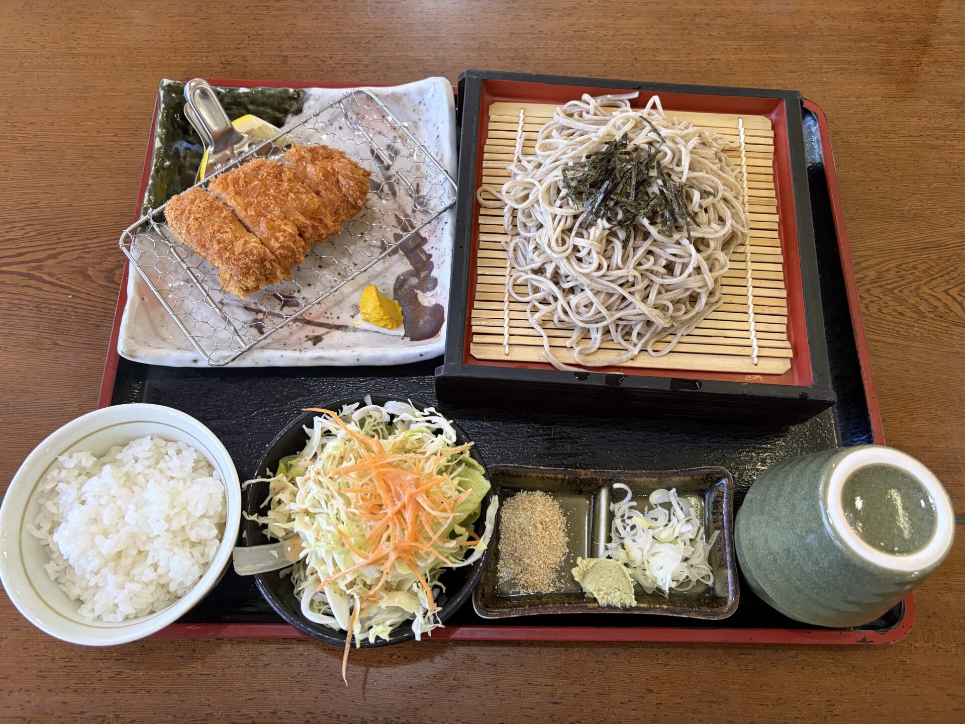 ロースかつ定食セット全景。金網に載ったロースかつ・ざるそば・ご飯・キャベツ