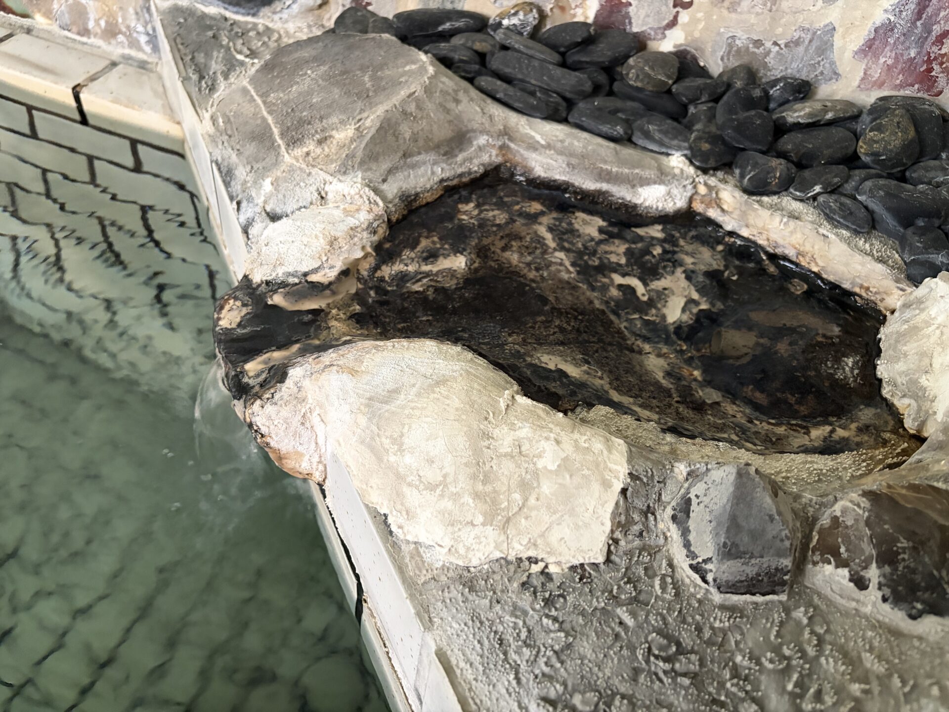 内湯の湯口。白い析出物がびっしり付いた石組みと黒石