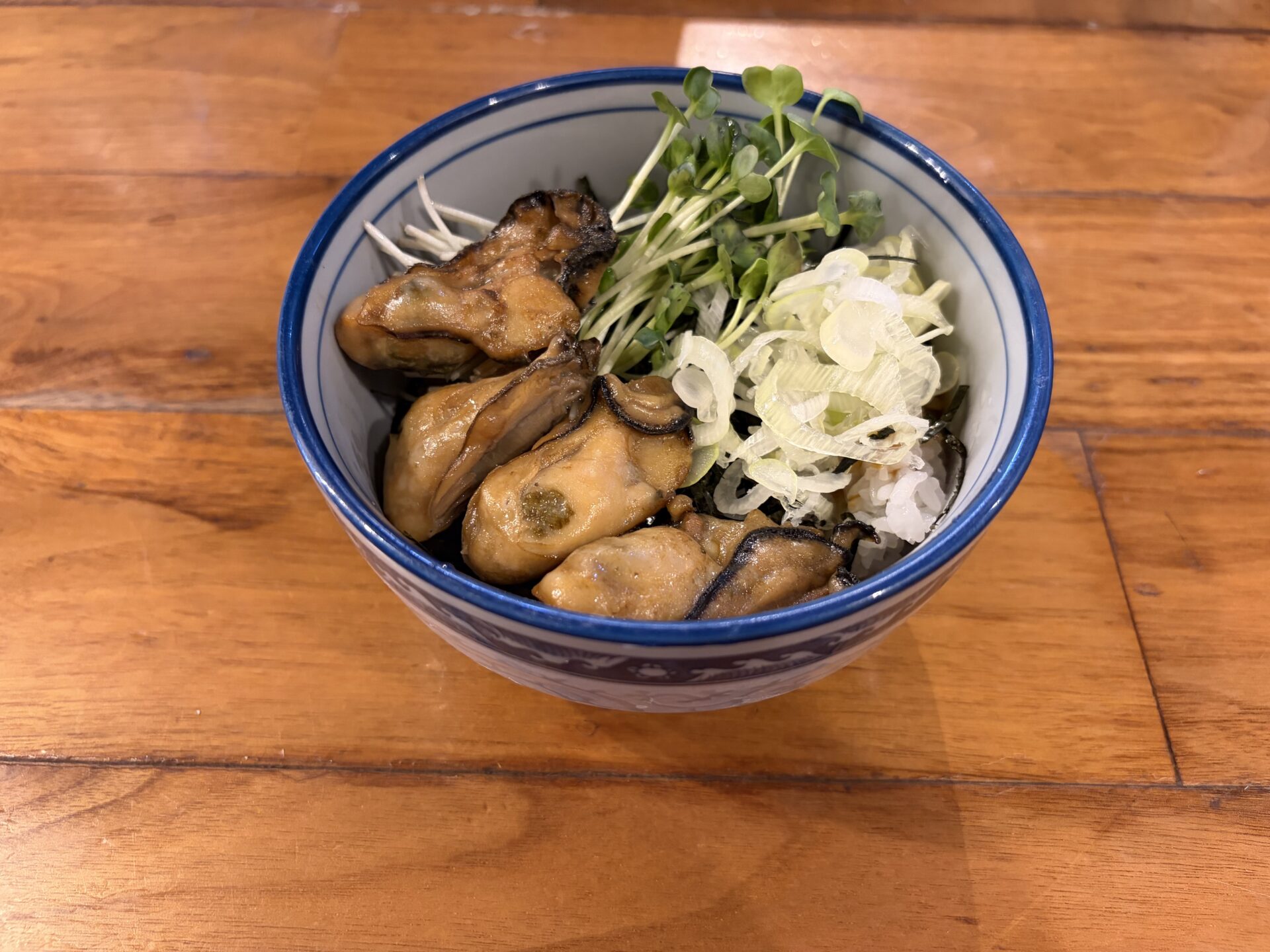 牡蠣めし。タレ色に染まった牡蠣がごろごろと載り、刻み海苔・白ねぎ・かいわれが覆う