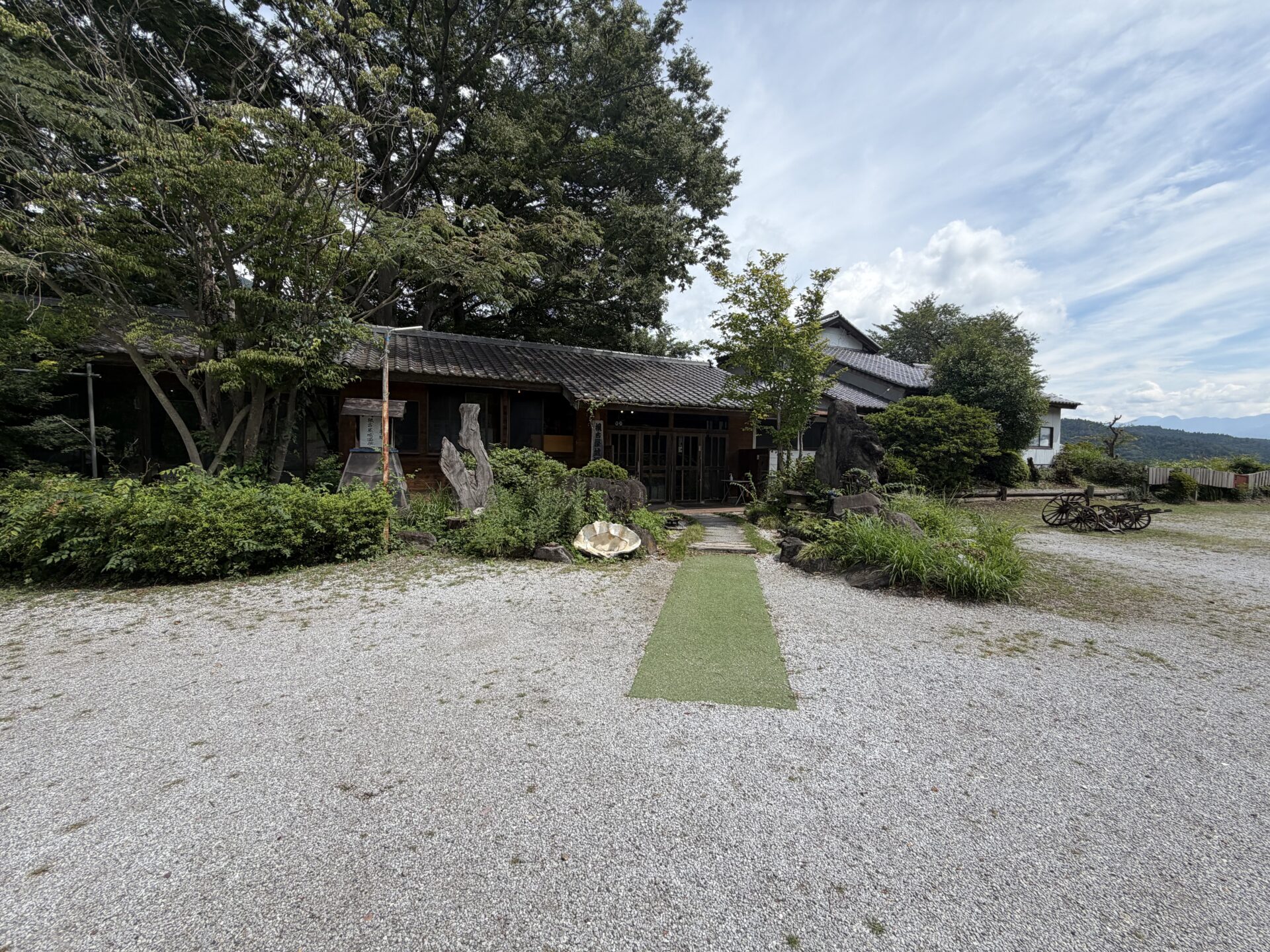 砂利の広場の先に建つ瓦屋根の平屋。緑のカーペットが玄関まで一直線に伸びる