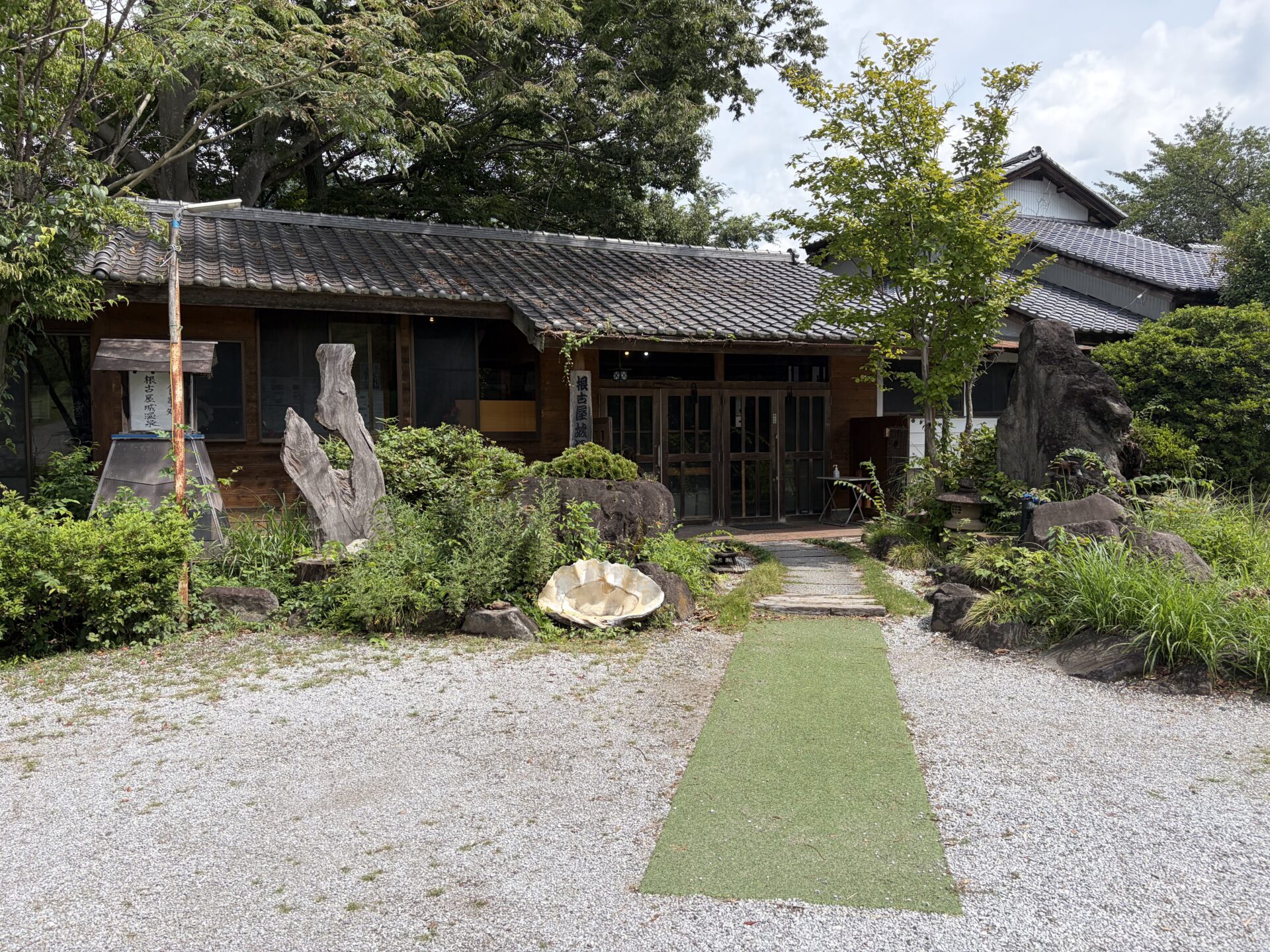 玄関まわり。流木のオブジェと巨石、木の縦看板「根古屋城温泉」