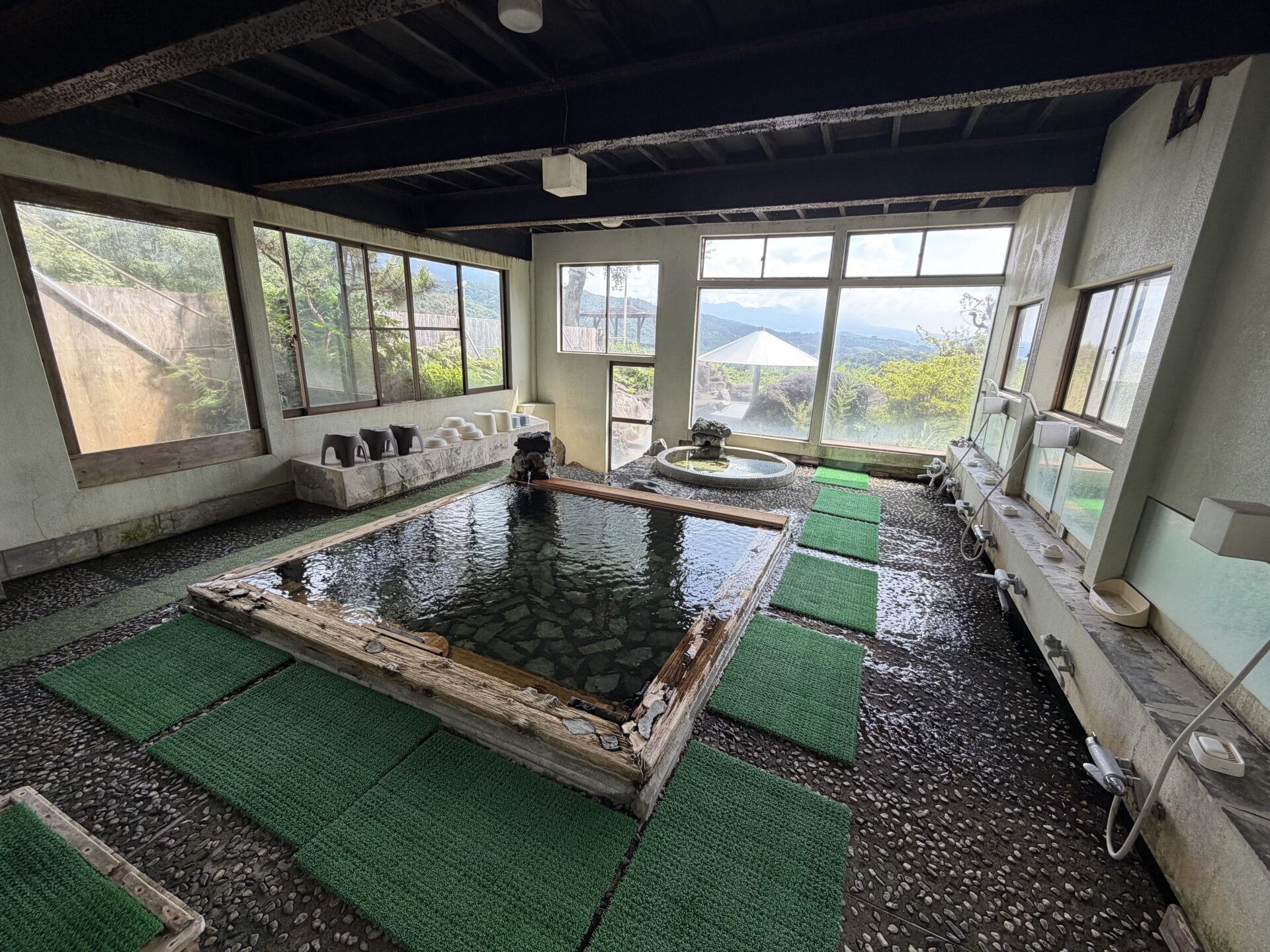 木枠の内湯。石張りの底まで透けて見える透明湯。大窓の外に露天と山並み