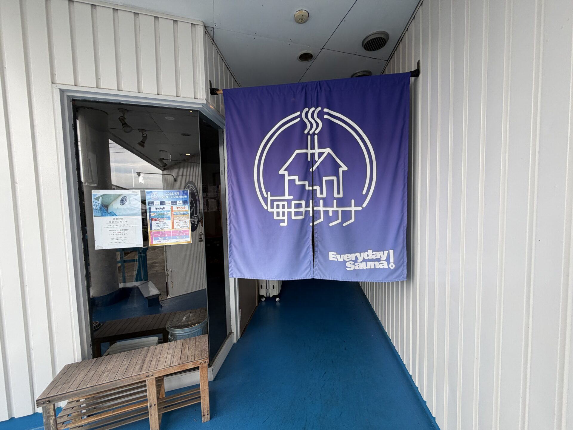 入口ののれん。窓に営業時間変更のお知らせと月間イベントカレンダーの掲示