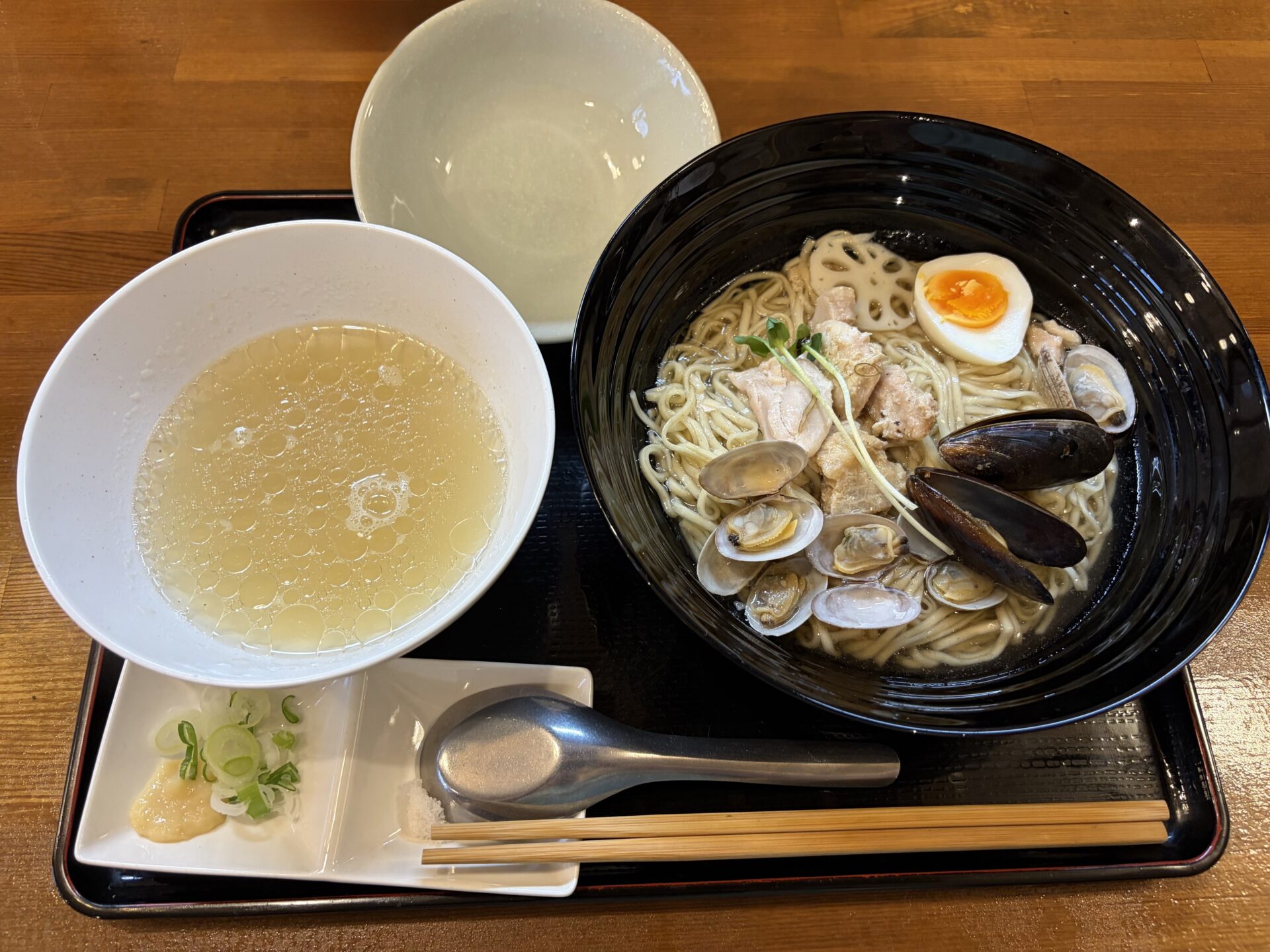貝出汁昆布水つけ麺(塩)。昆布水に浸った全粒粉麺にあさり・ムール貝・鶏肉、別椀に黄金色の貝出汁、小皿に藻塩と生姜。空の器は貝殻入れ