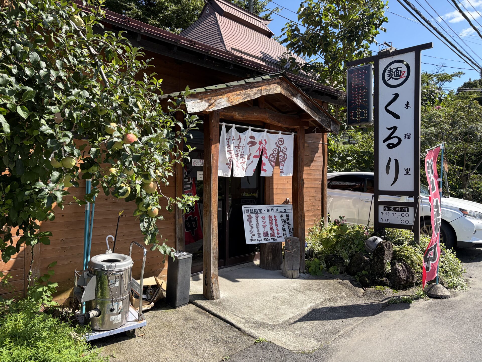 県道61号沿いの外観。木造の店先に実をつけた木、「麺z くるり」の看板と期間限定メニューのボード