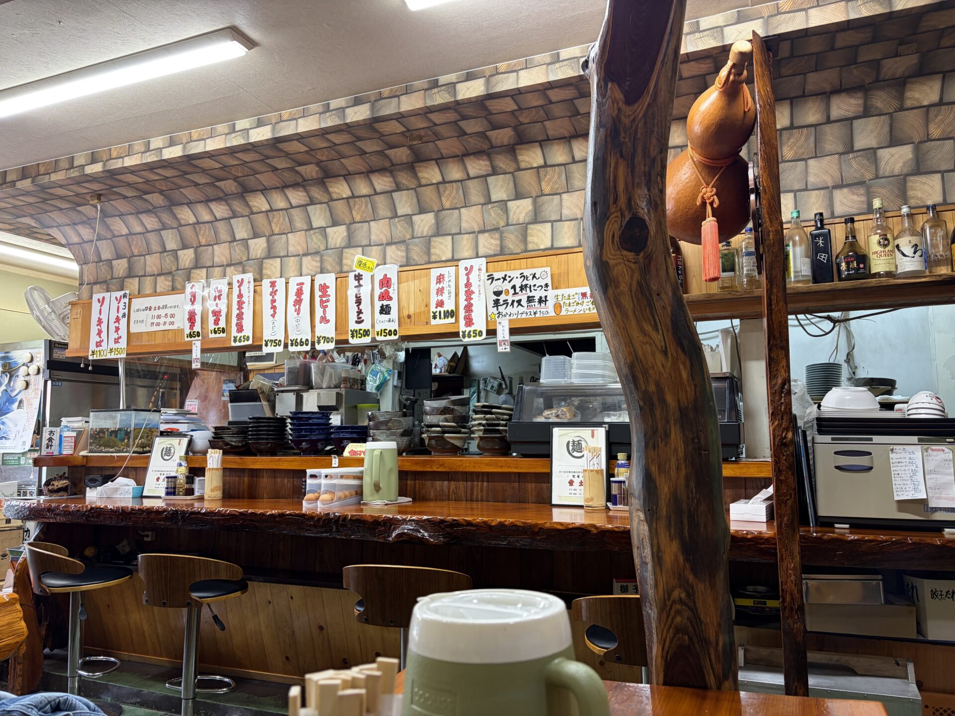 カウンター越しに壁の短冊。ソーキそば、肉塊麺、麻辣麺、「半ライス無料」「生たまご無料」