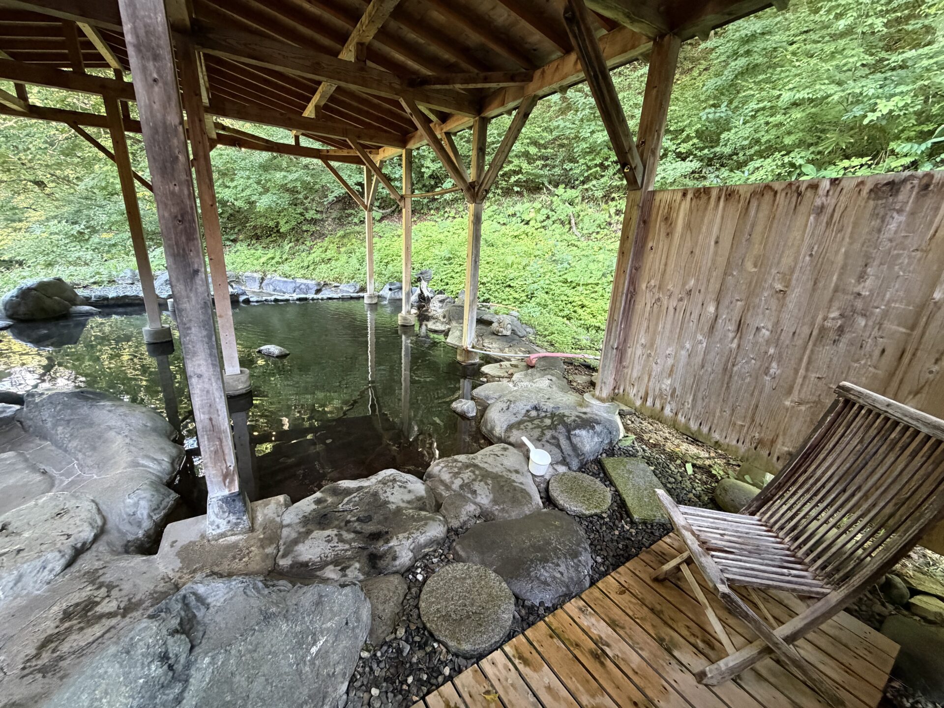 大龍。木の屋根の下に大きな岩風呂、奥は山の緑。デッキチェアが1脚