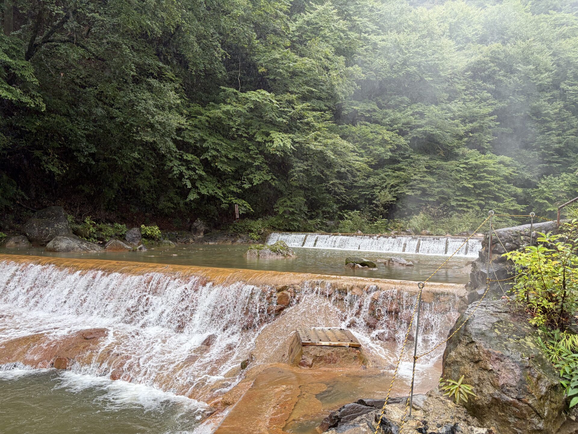 川をせき止めた堰。縁が赤茶に色づき、雨の中でも湯気が上がっていた