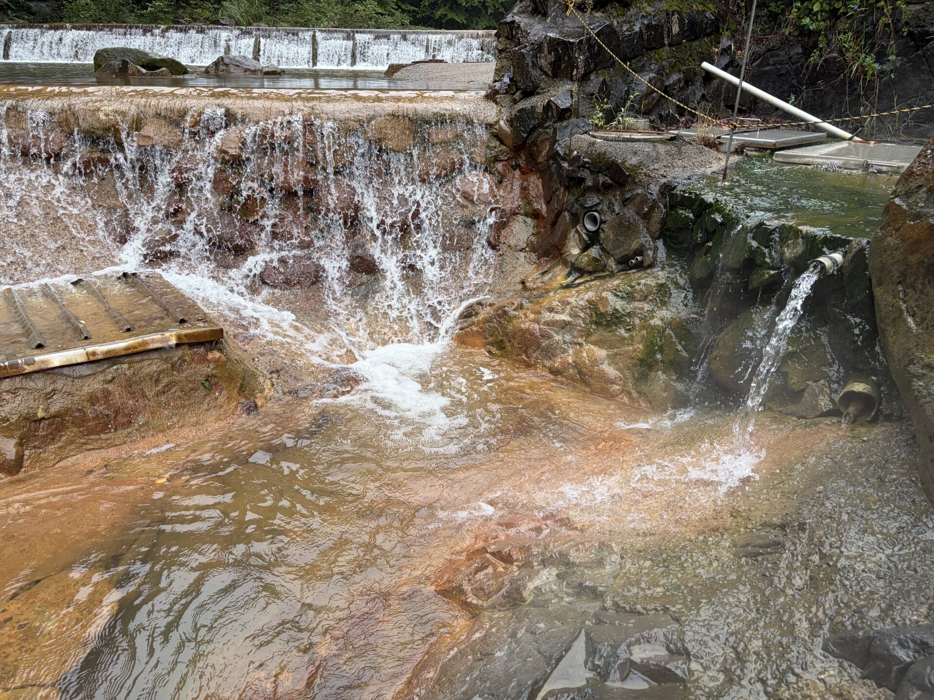 岩の間の配管から熱い湯が落ちる。鉄格子の下の水路と合流する