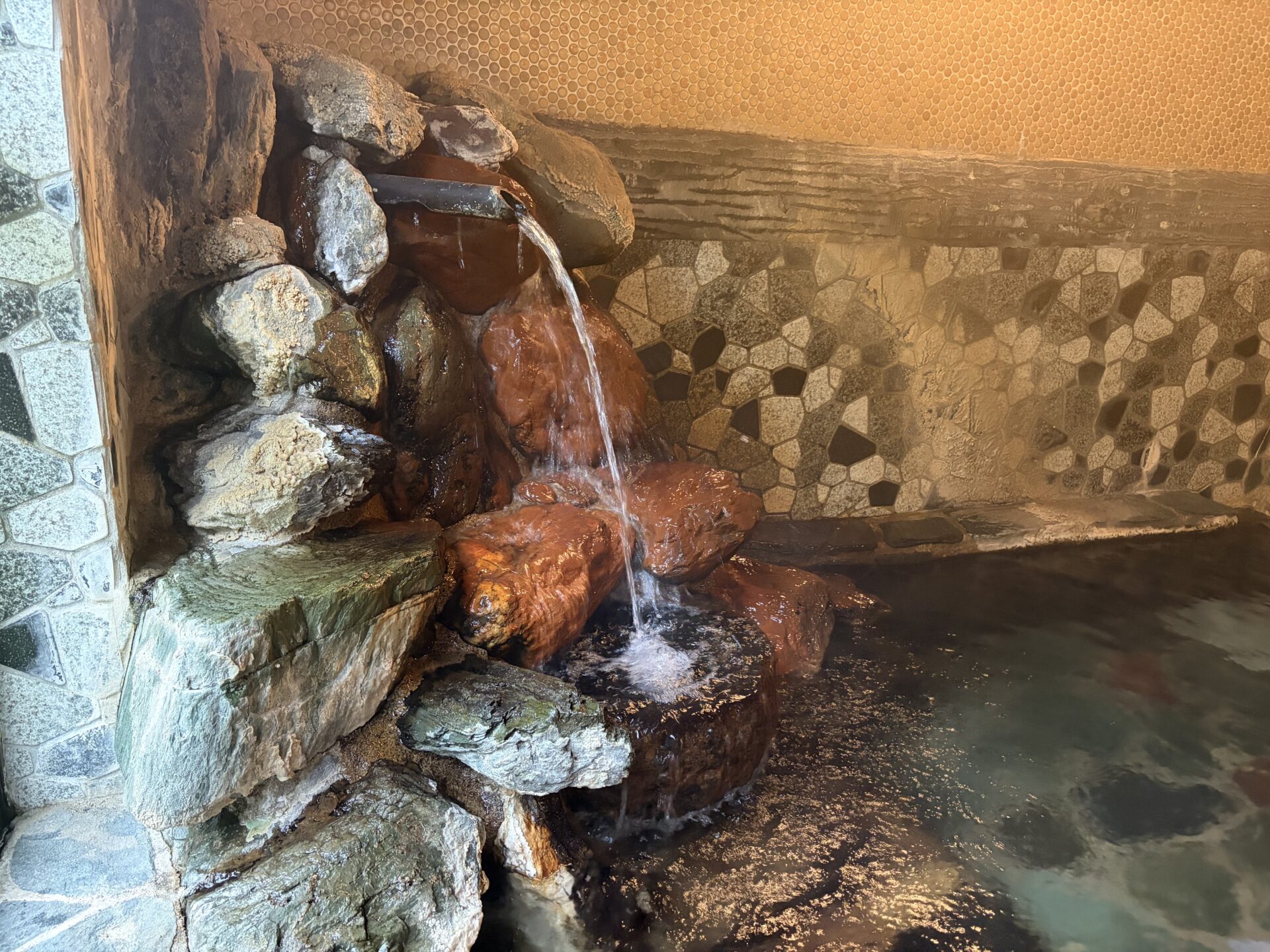 内湯の湯口。竹筒から落ちる湯で、下の岩が赤茶に染まっている