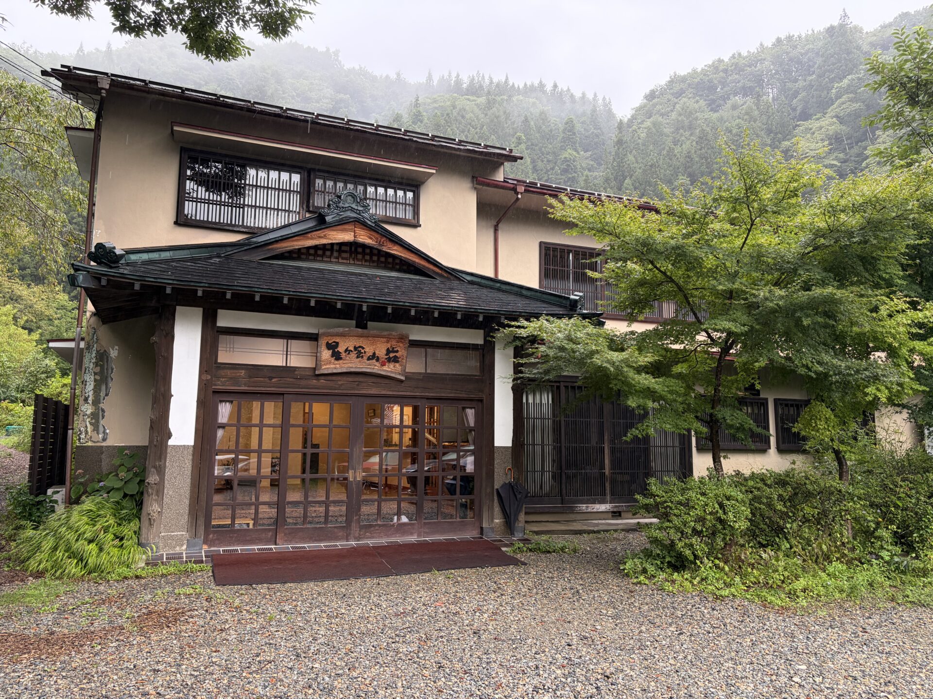 星ヶ岡山荘の外観。雨に濡れた砂利の前庭と、木の看板