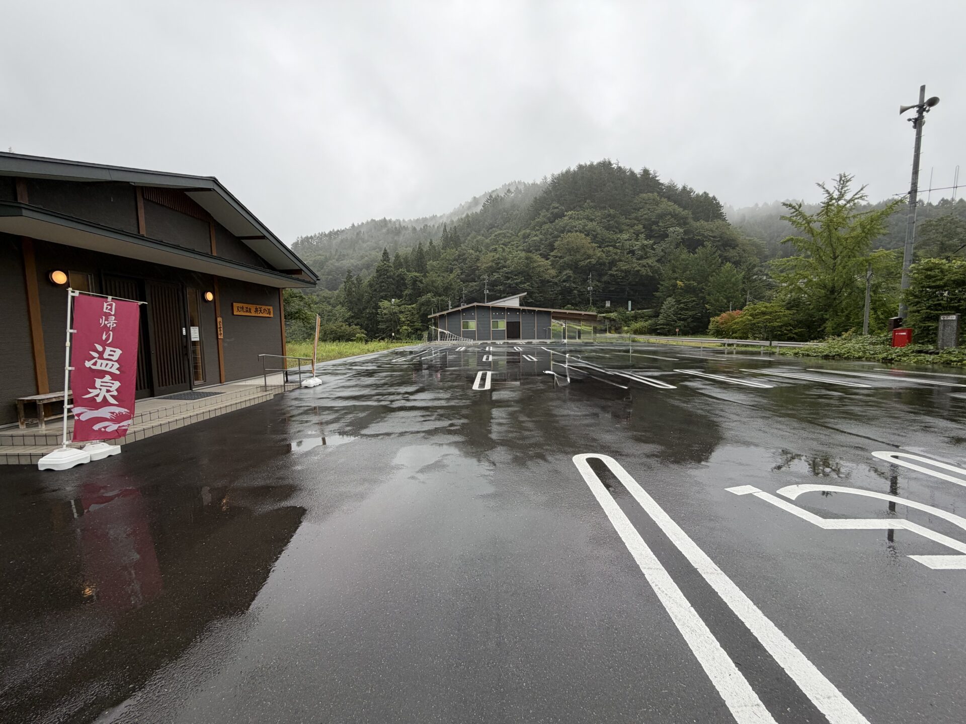 広い駐車場。雨に濡れた白線の向こうに山並み