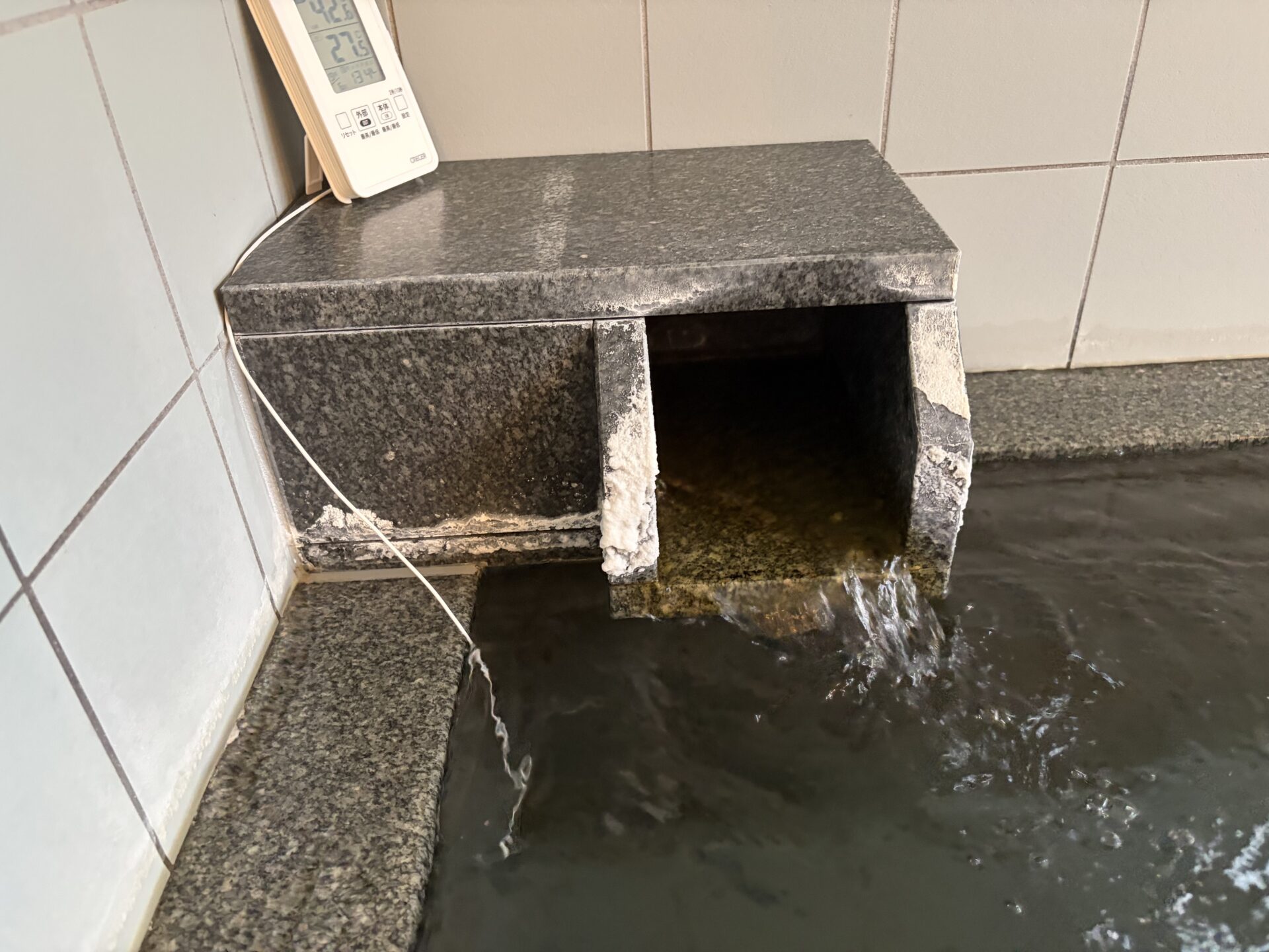 御影石の湯口から浴槽に流れ込む湯。縁には白い付着物