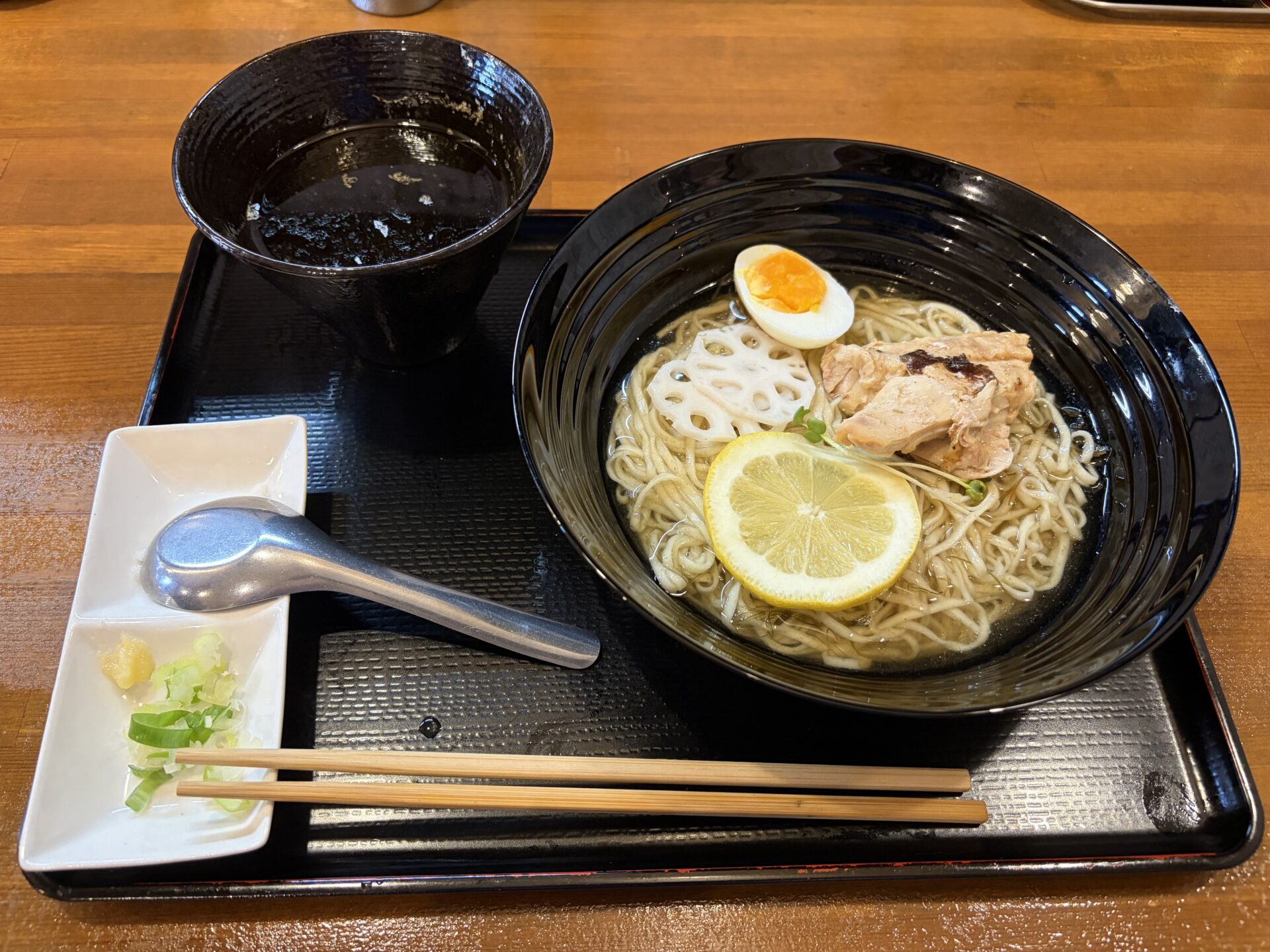 鶏昆布水つけ麺(醤油)。昆布水に浸った麺に柑橘の輪切り、蓮根、鶏肉、半熟卵。黒い器が醤油のつけ汁